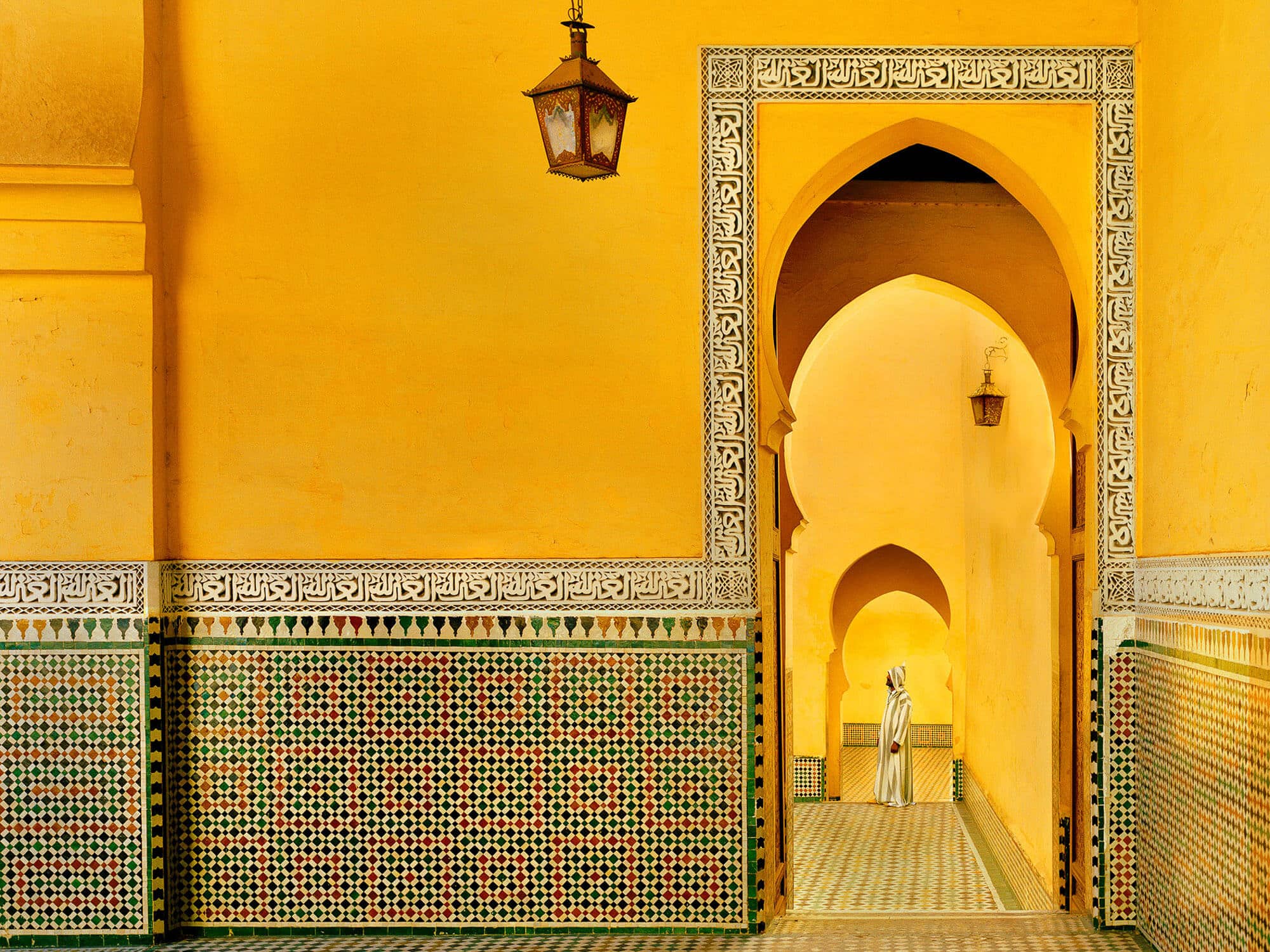 Man standing beneath arch in bright yellow Meknes courtyard