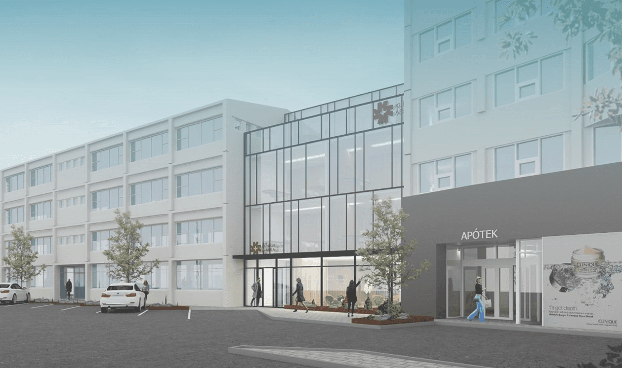 Two doctors in white lab coats and stethoscopes standing confidently in a clinical setting with medical posters and a bed in the background