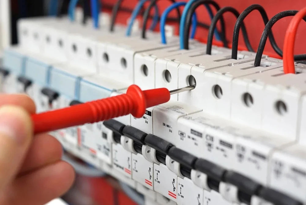 Electrical testing being carried out on a circuit breaker panel using a multimeter probe.