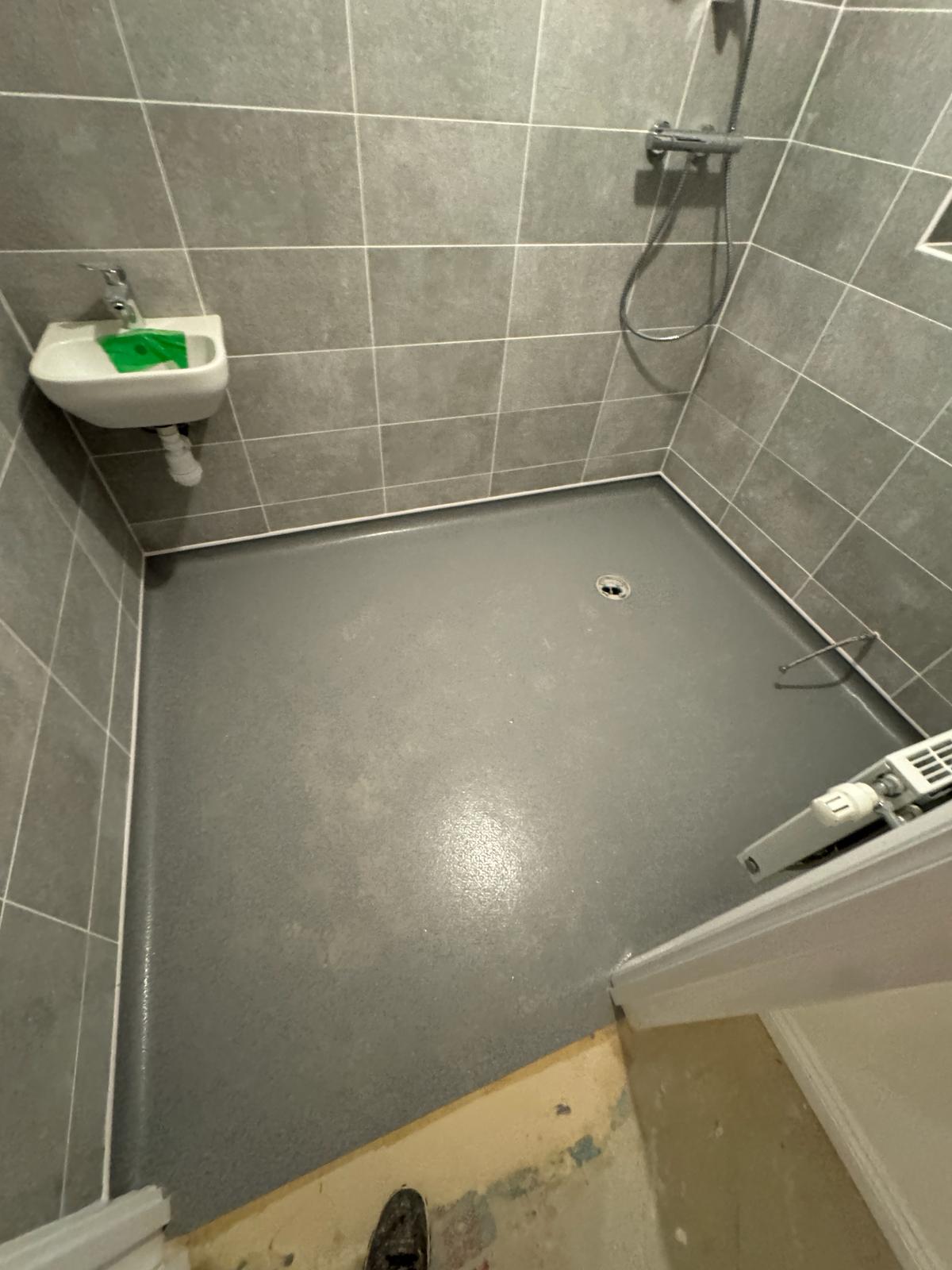 A modern wet room features slip-resistant safety flooring in a sleek gray shade, with expertly fitted tiles lining the walls and a compact basin and shower fixture, ideal for a stylish and functional bathroom.