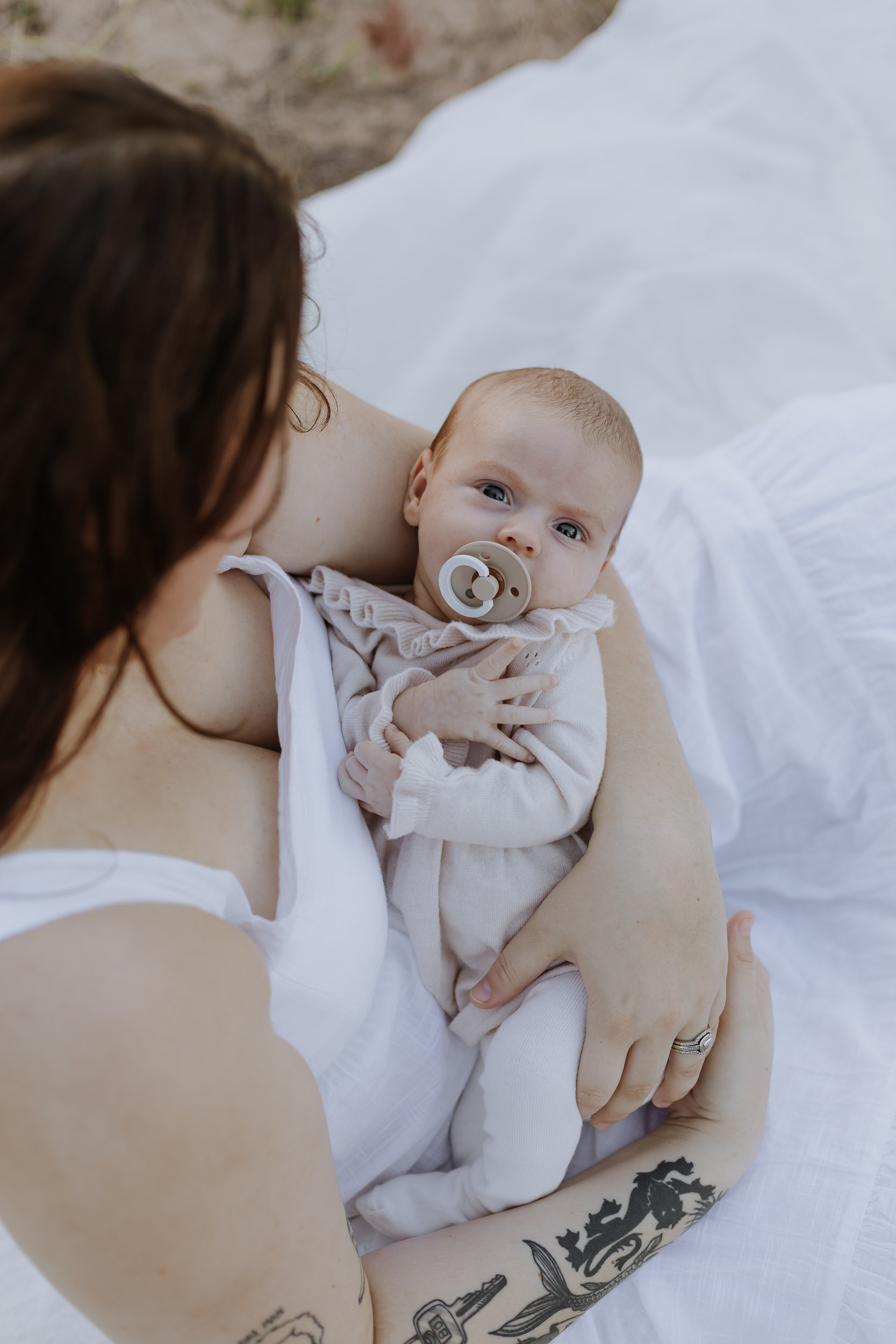 Arial view of baby held in mother's arms while sitting in the grass at sunset outdoor photoshoot in Mackay
