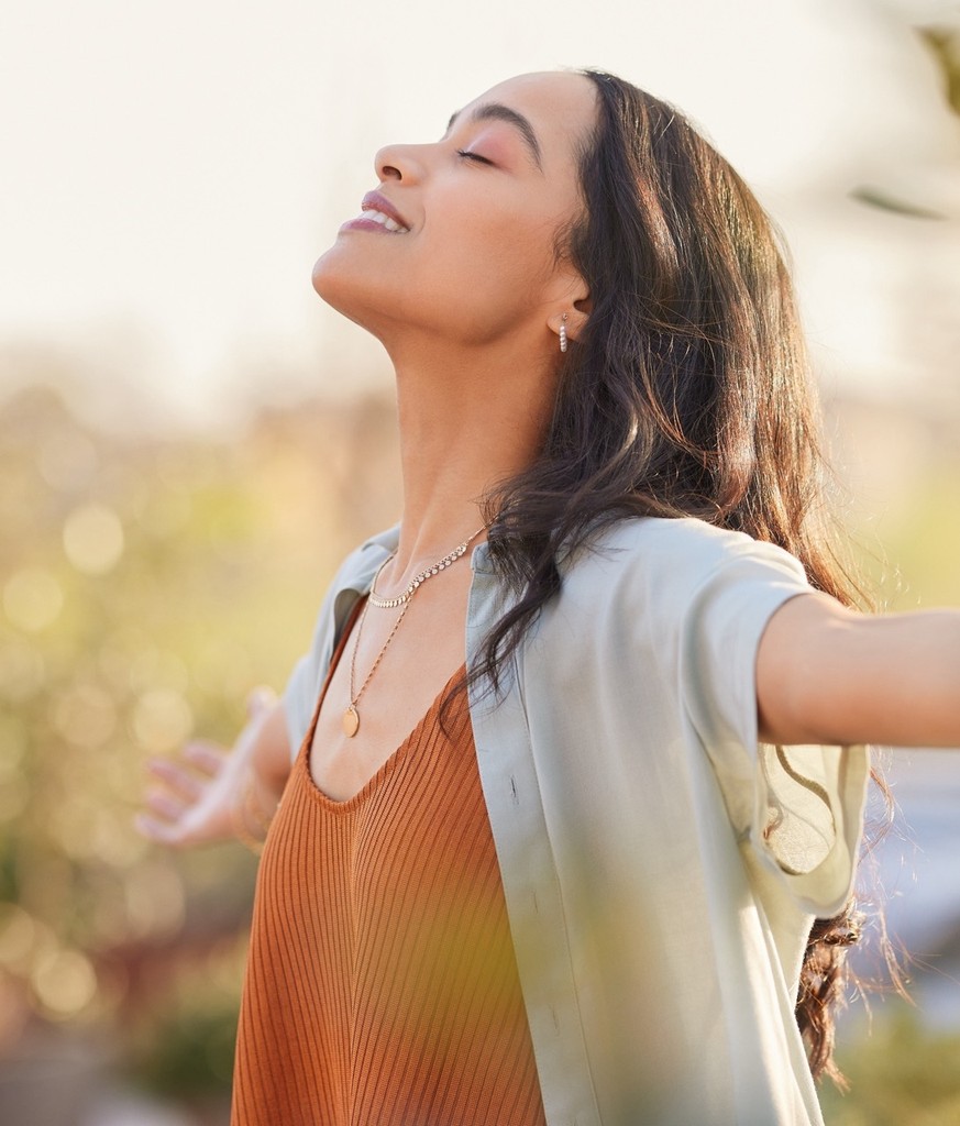 Peaceful woman outdoors with her eyes closed, practicing mindfulness in soft natural light.