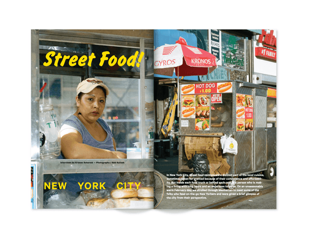 An open magazine spread displays two photographs of New York City street food vendors. On the left, a woman wearing a cap stands behind a glass display case with “Street Food!” in yellow text. On the right, a food cart with a red and white striped awning is parked on a city street. The cart advertises “HOT DOG 11.00” and “KRONOS,” with a man visible inside. The text below the images reads “NEW YORK CITY.”