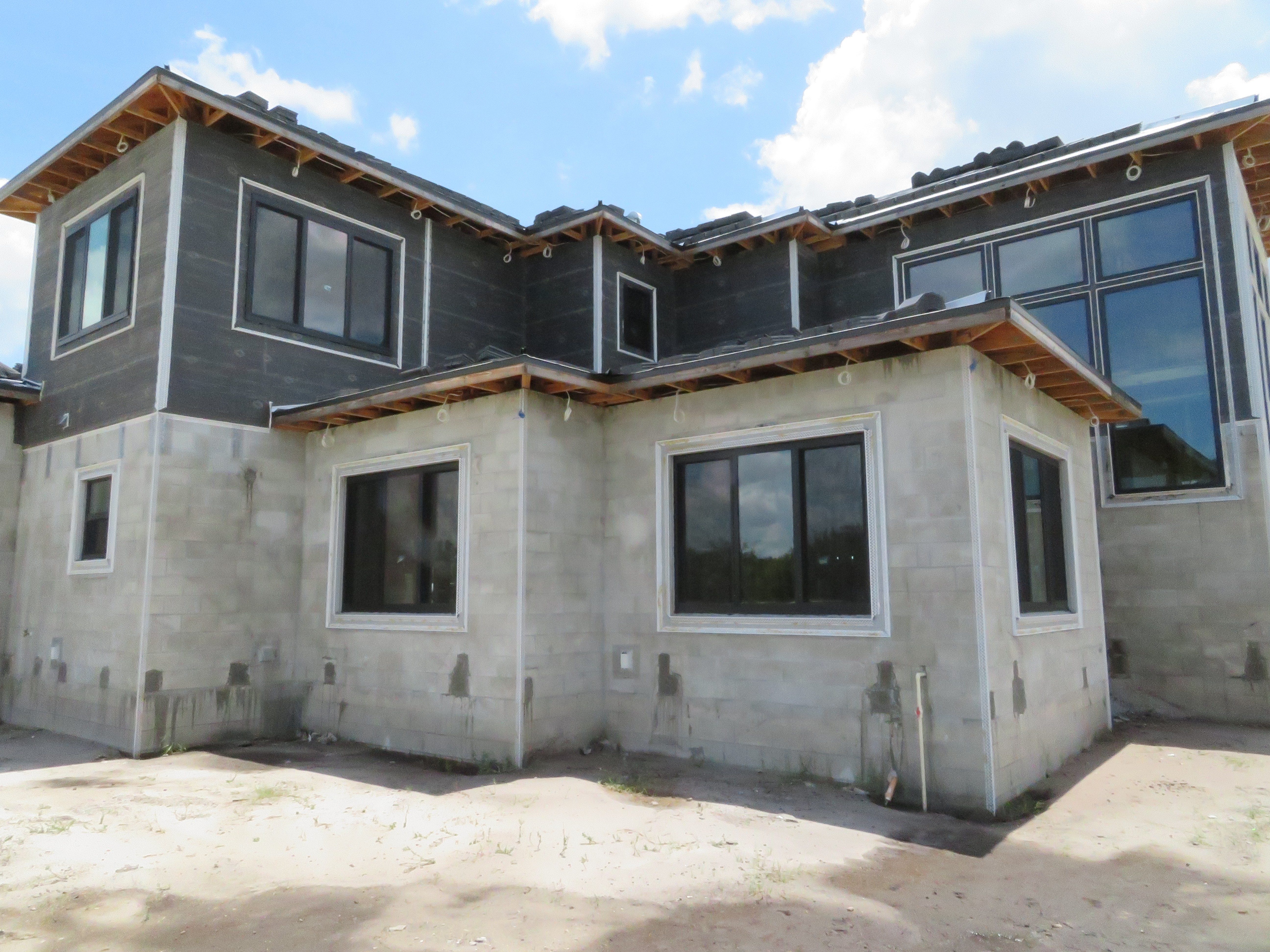 Construction of a modern house with concrete walls and dark windows, showing framing and roofing.