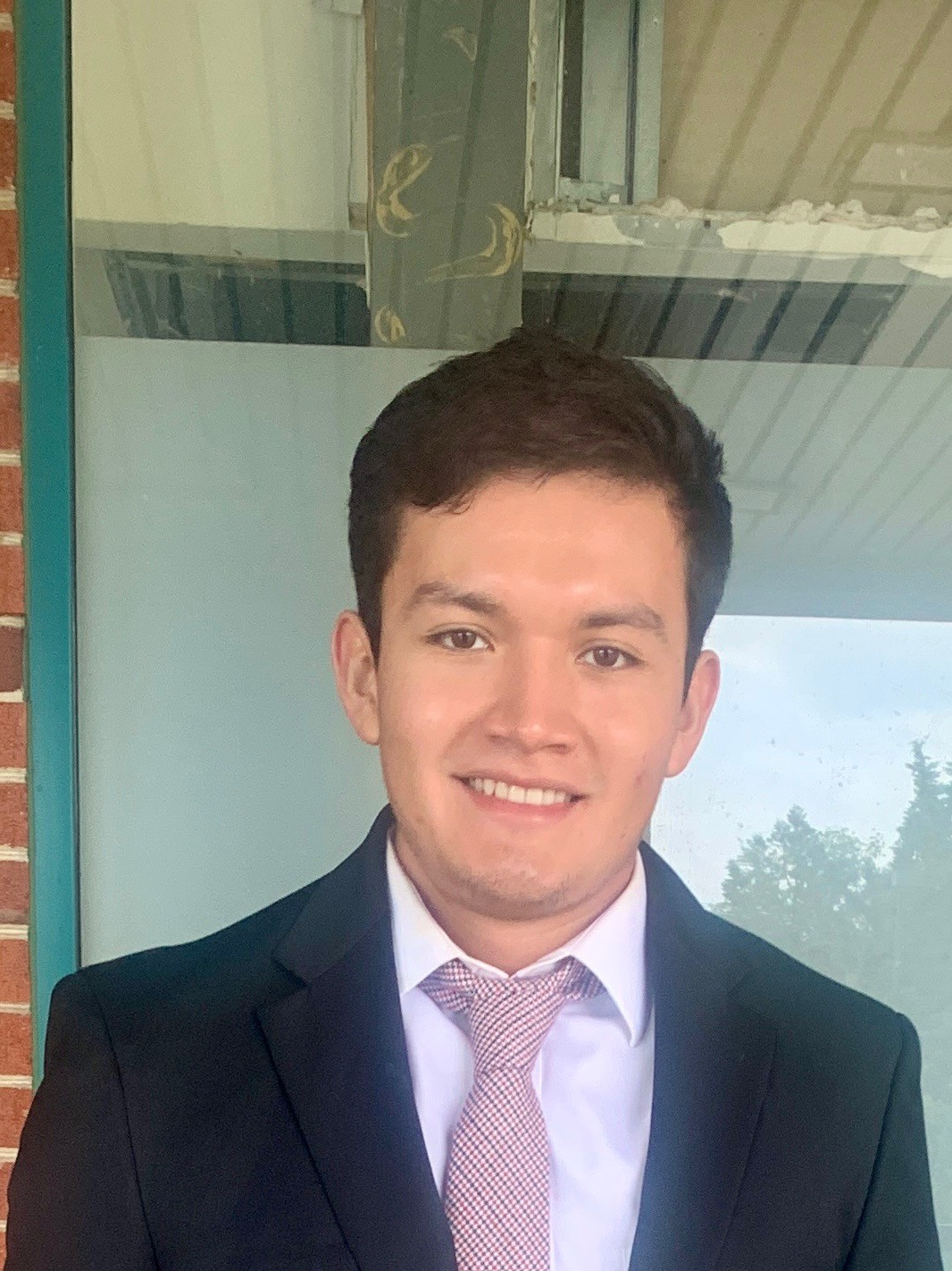 Portrait of a young woman with dark hair and green eyes, wearing a black top and gold necklace, set against a neutral background.