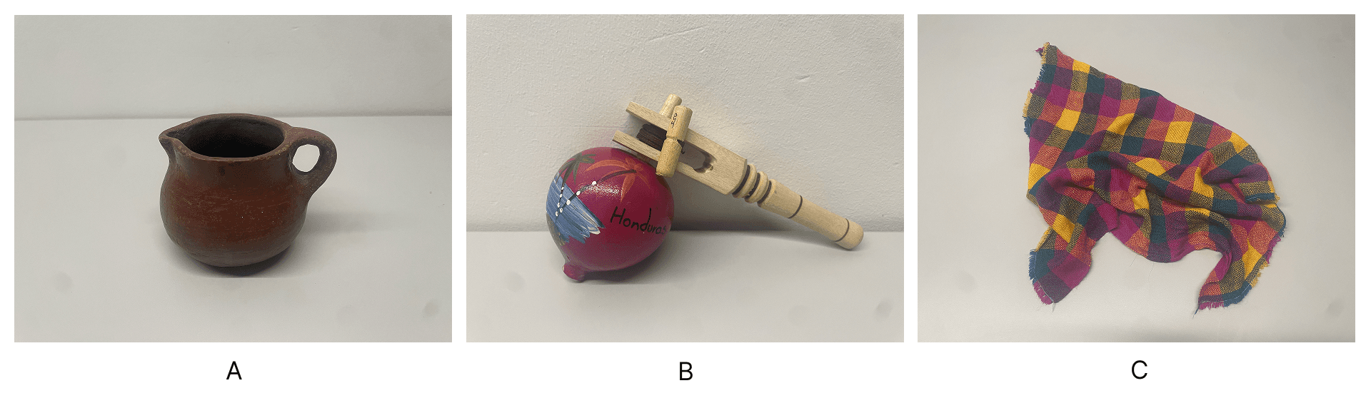 Three photographs of Honduran cultural artifacts arranged side by side on a white background. Panel A shows a small brown earthenware pocillo made of clay with a single handle. Panel B shows a painted wooden trompo (spinning top) resting on its side with an attached wooden winder and string. Panel C shows a crumpled multicolored woven cloth in magenta, yellow, green, and blue tones.