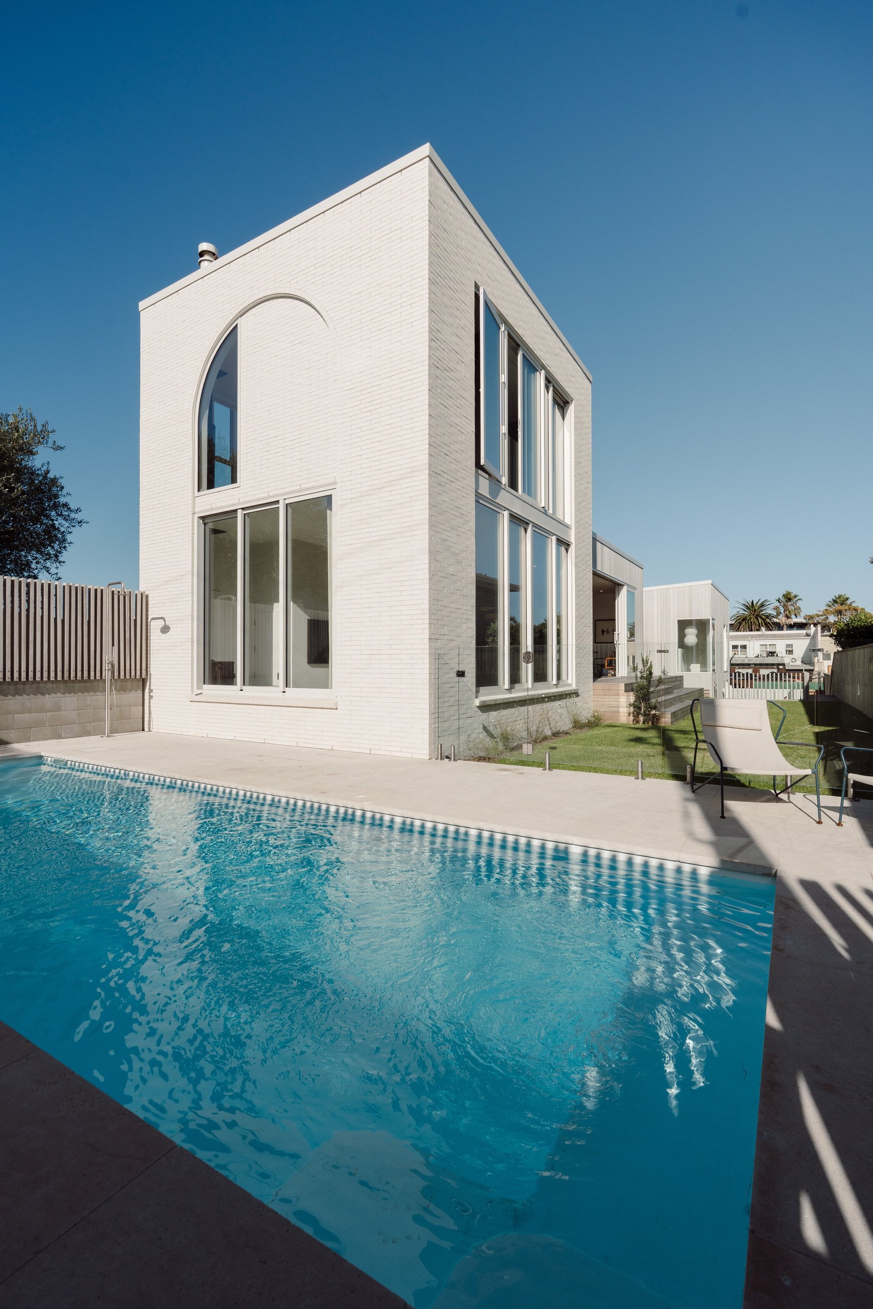 White rendered home with an arched window beside a swimming pool