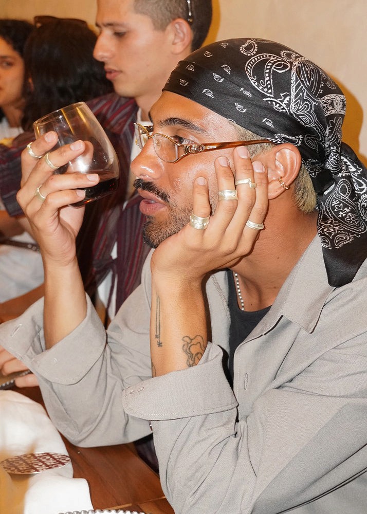 Man with multiple rings showing off his silver jewelry in a casual setting with people in the background