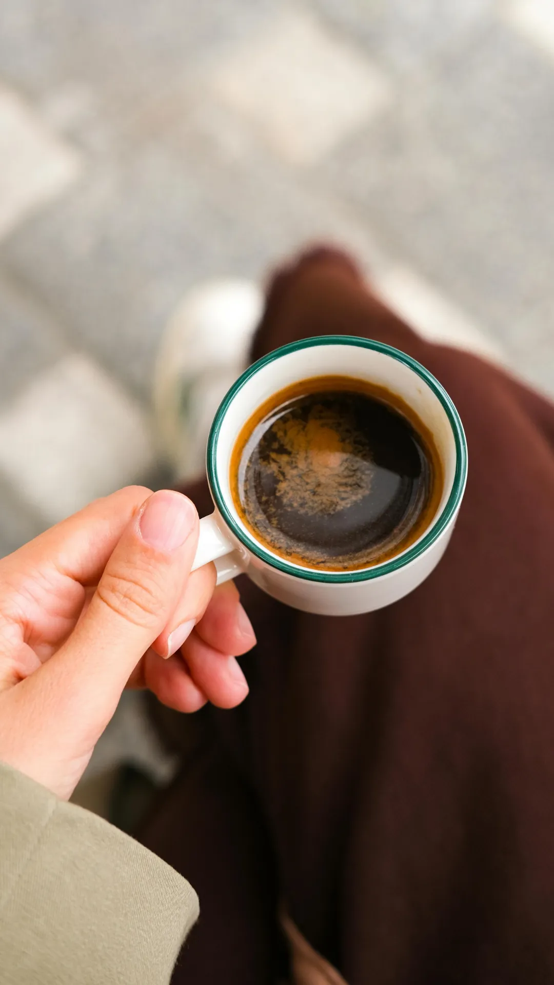 A person holding a steaming cup of coffee, with a relaxed expression, sitting at a table.