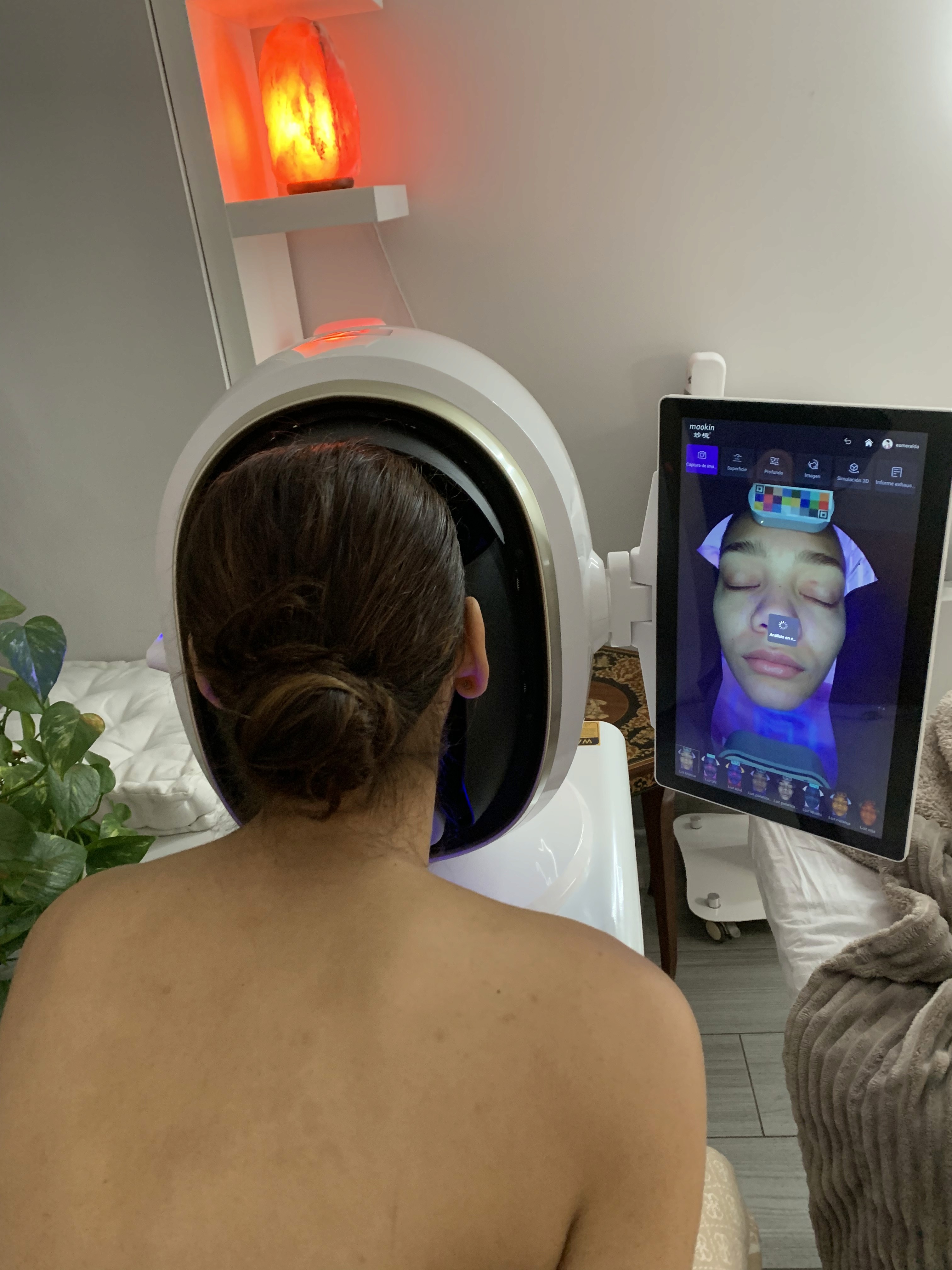 A woman lying down with a towel wrapped around her head, her face glowing with facial oil. She has a peaceful expression, enjoying a skincare treatment.