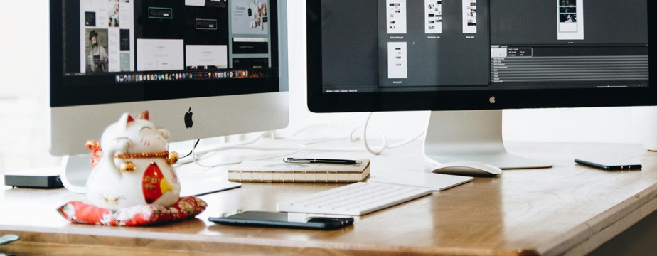 Desktop workspace with computer, lucky cat figurine, notebook, and coffee representing UX design work