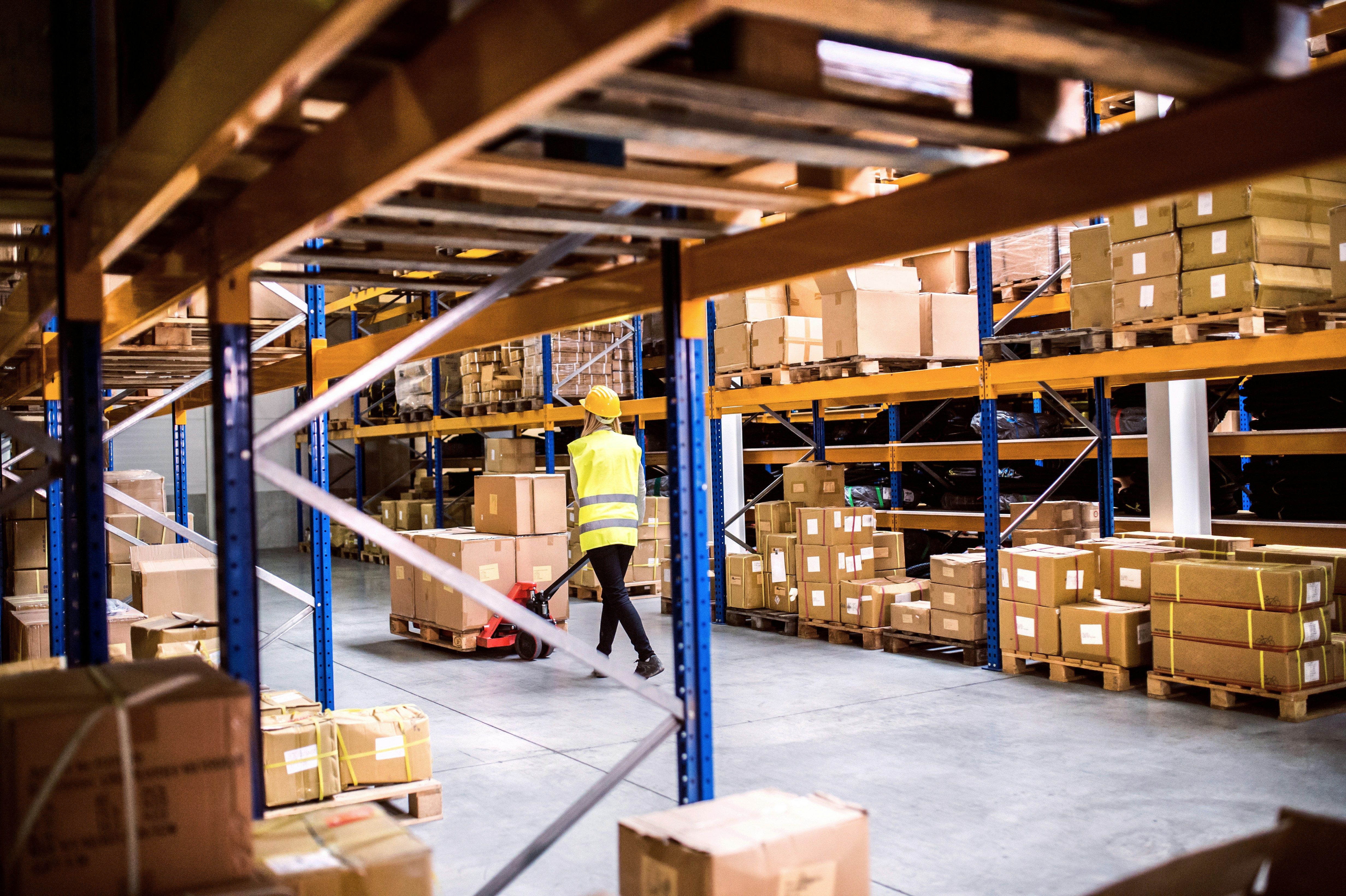 woman walking down warehouse aisle with pallet truck