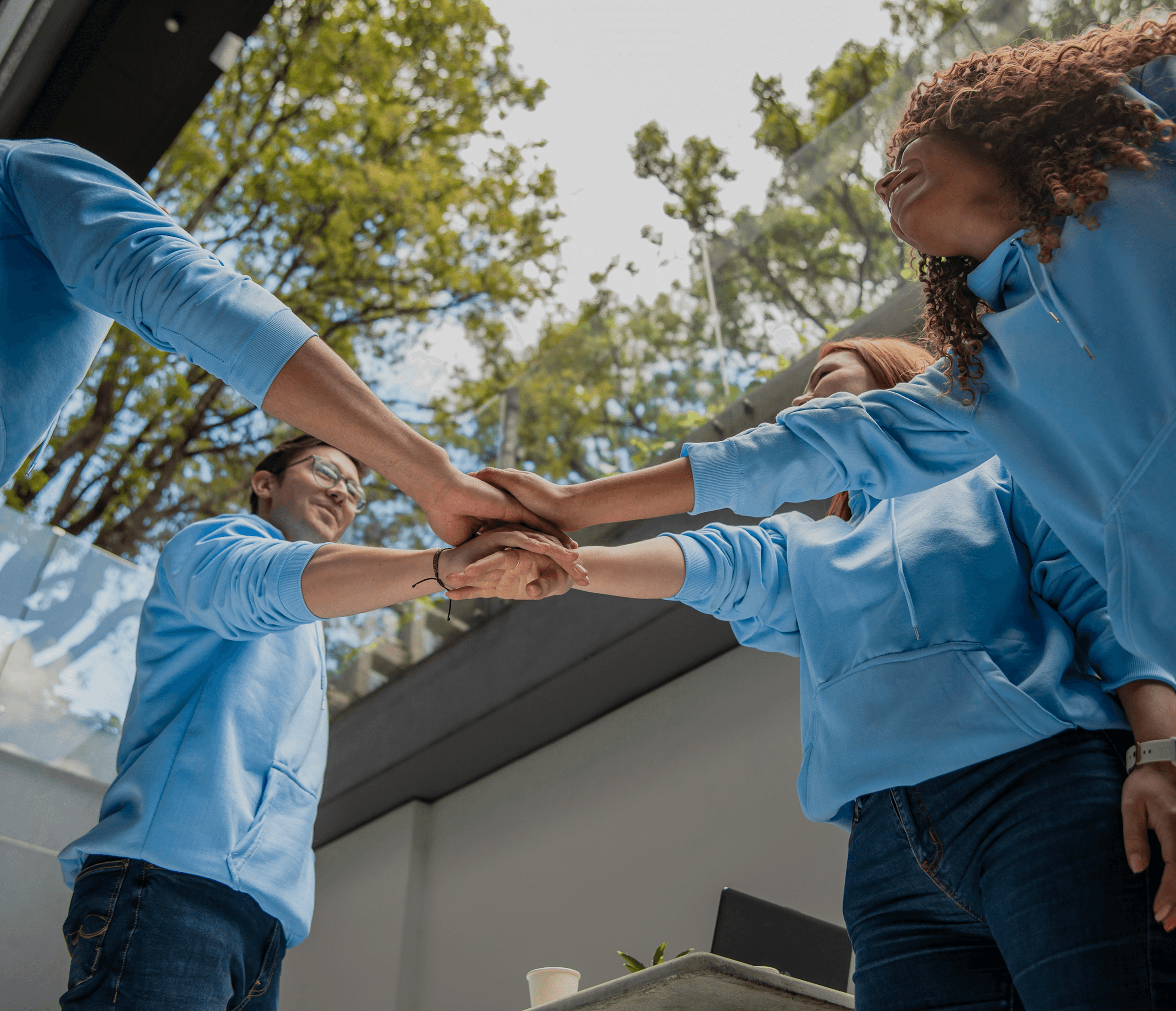 our people in light blue hoodies putting their hands together outside, symbolizing teamwork and unity.