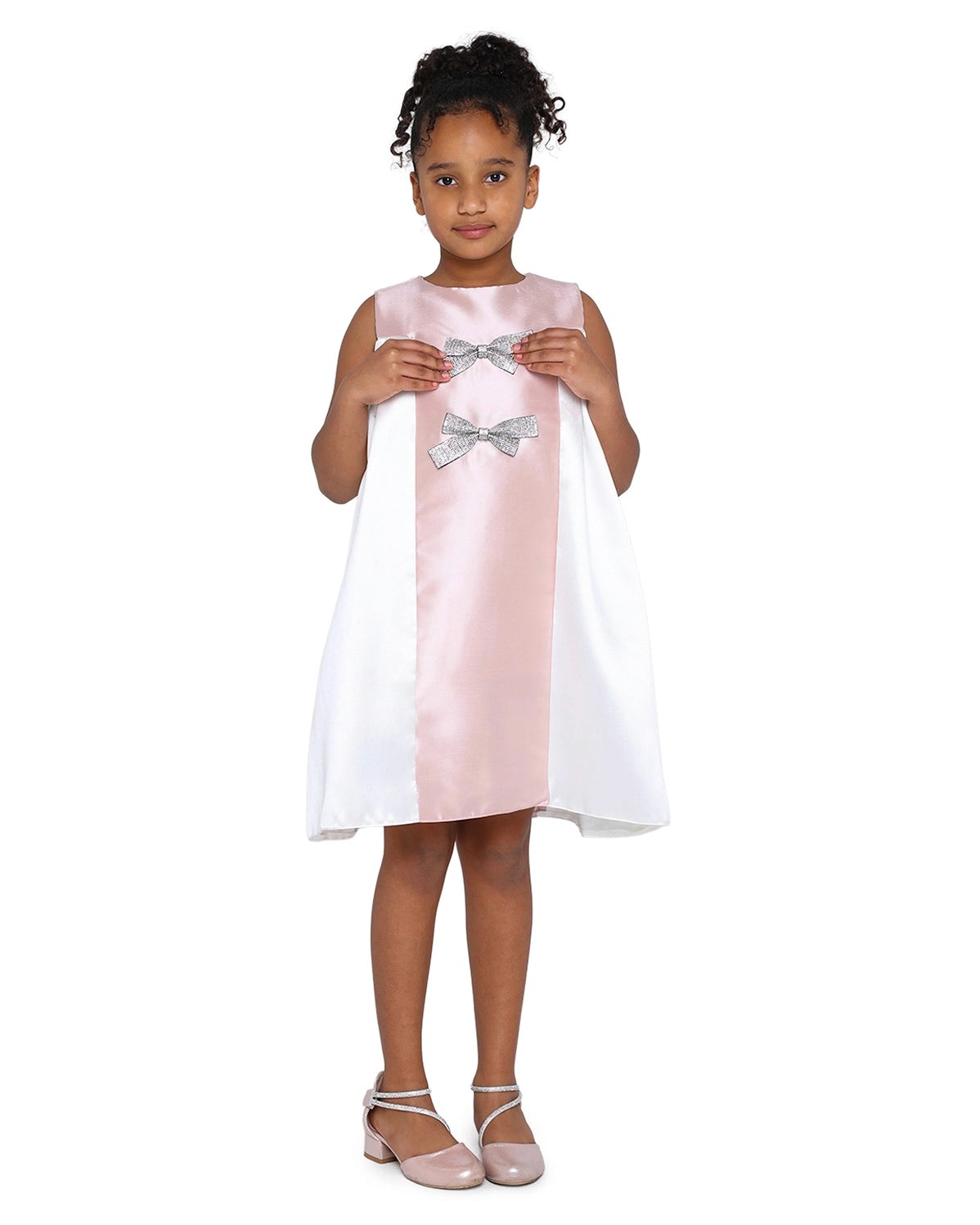 Young girl wearing a white dress with pink accents and silver bows on a white background