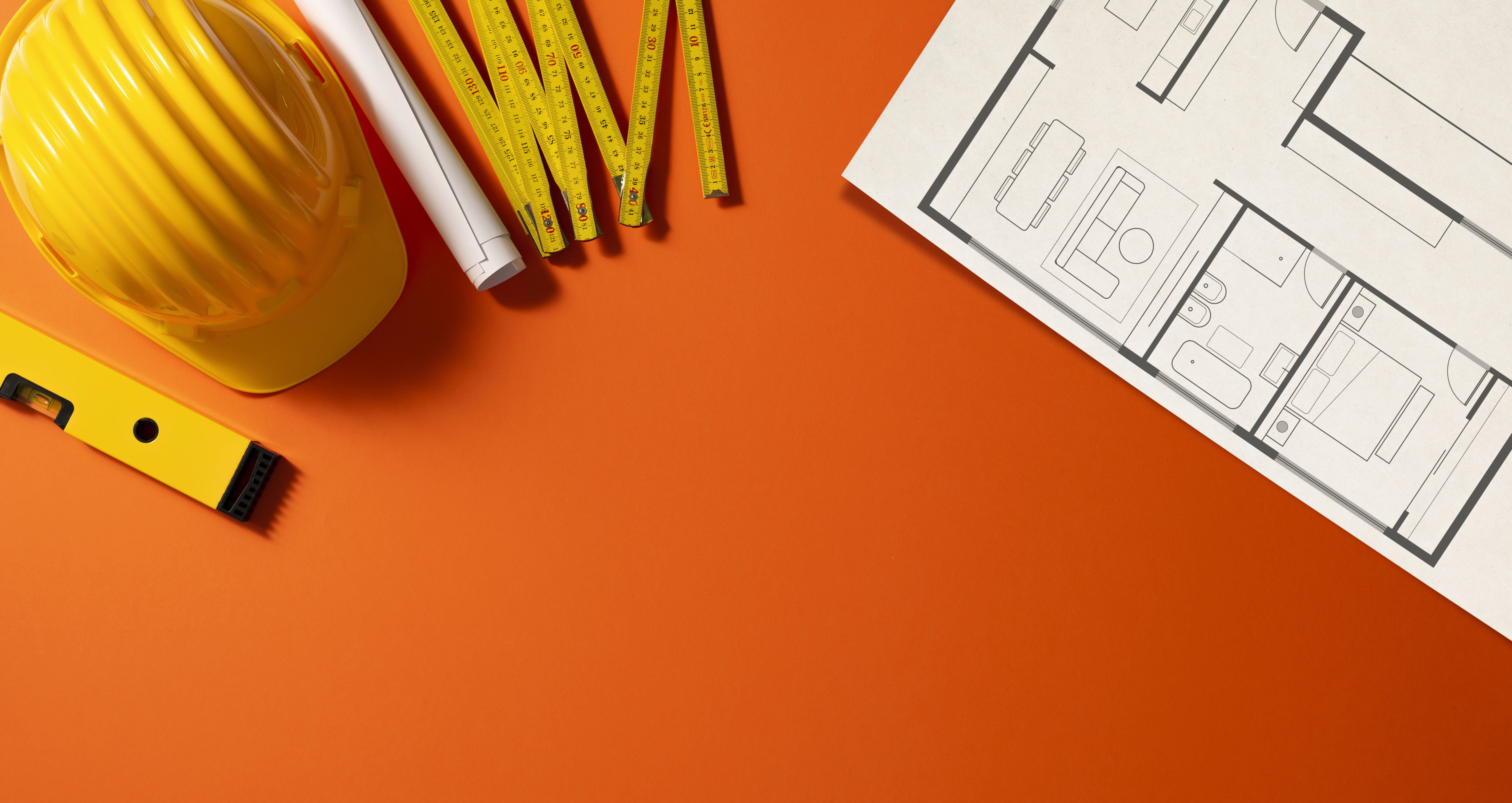 Top view of construction tools including a yellow hard hat, level, measuring tape, and architectural blueprint on an orange background.