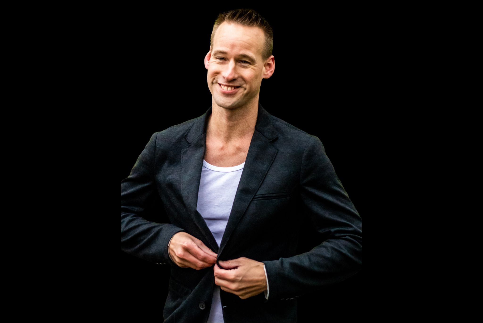 Danny van Brussel, high-end personal trainer voor ondernemers, in zwart colbert met lichte shirt, glimlachend tegen een donkere achtergrond.