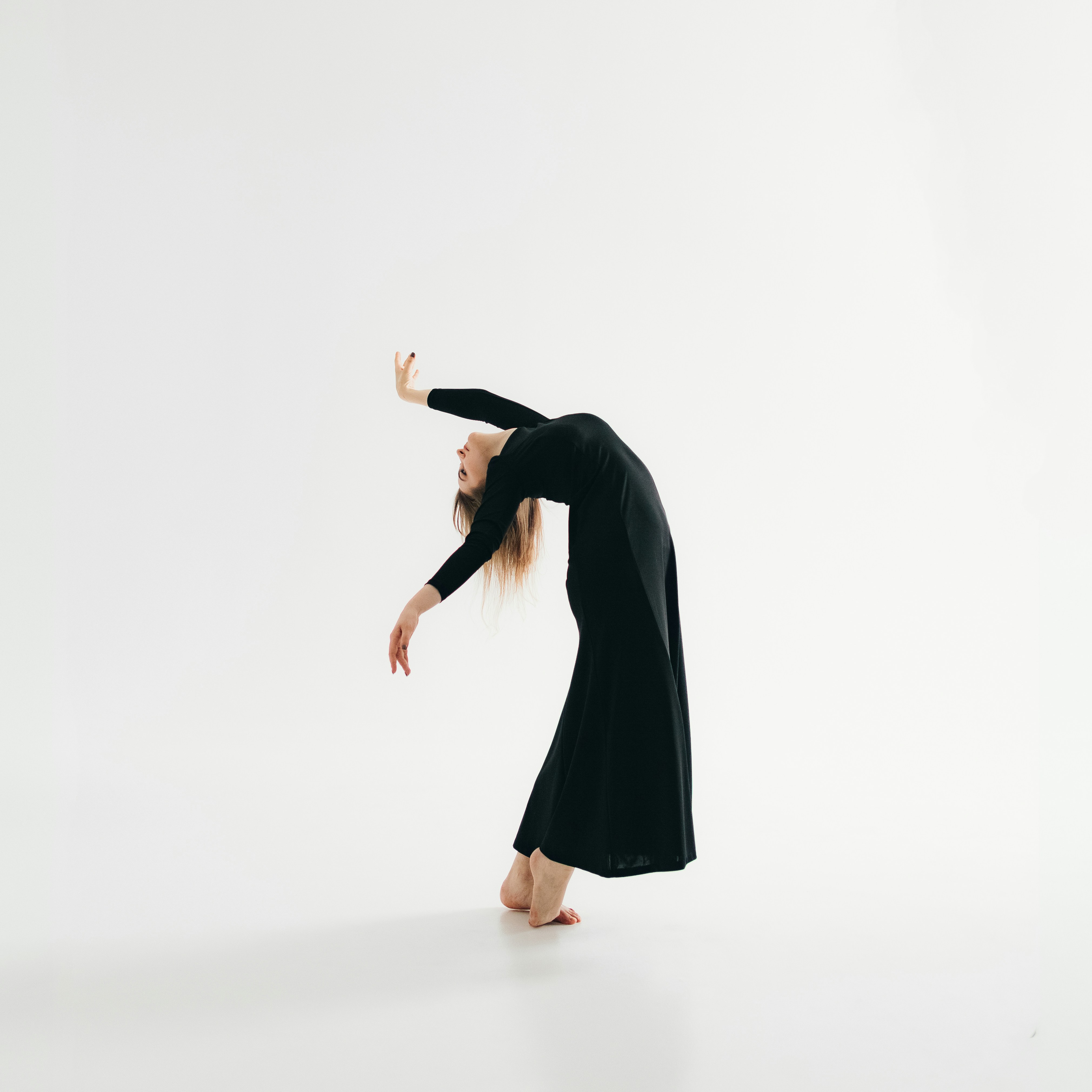 A person in a black dress bends backward gracefully against a plain white background.