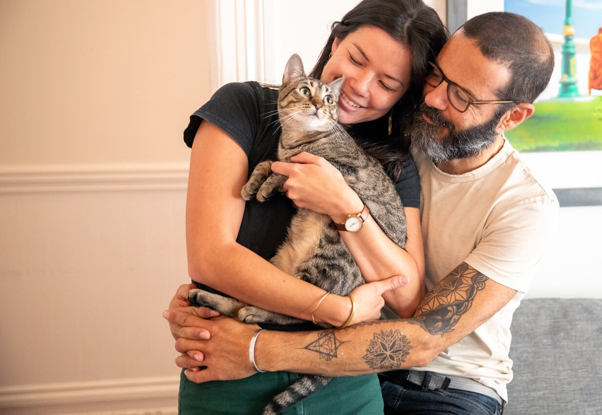 happy couple cuddling tabby cat