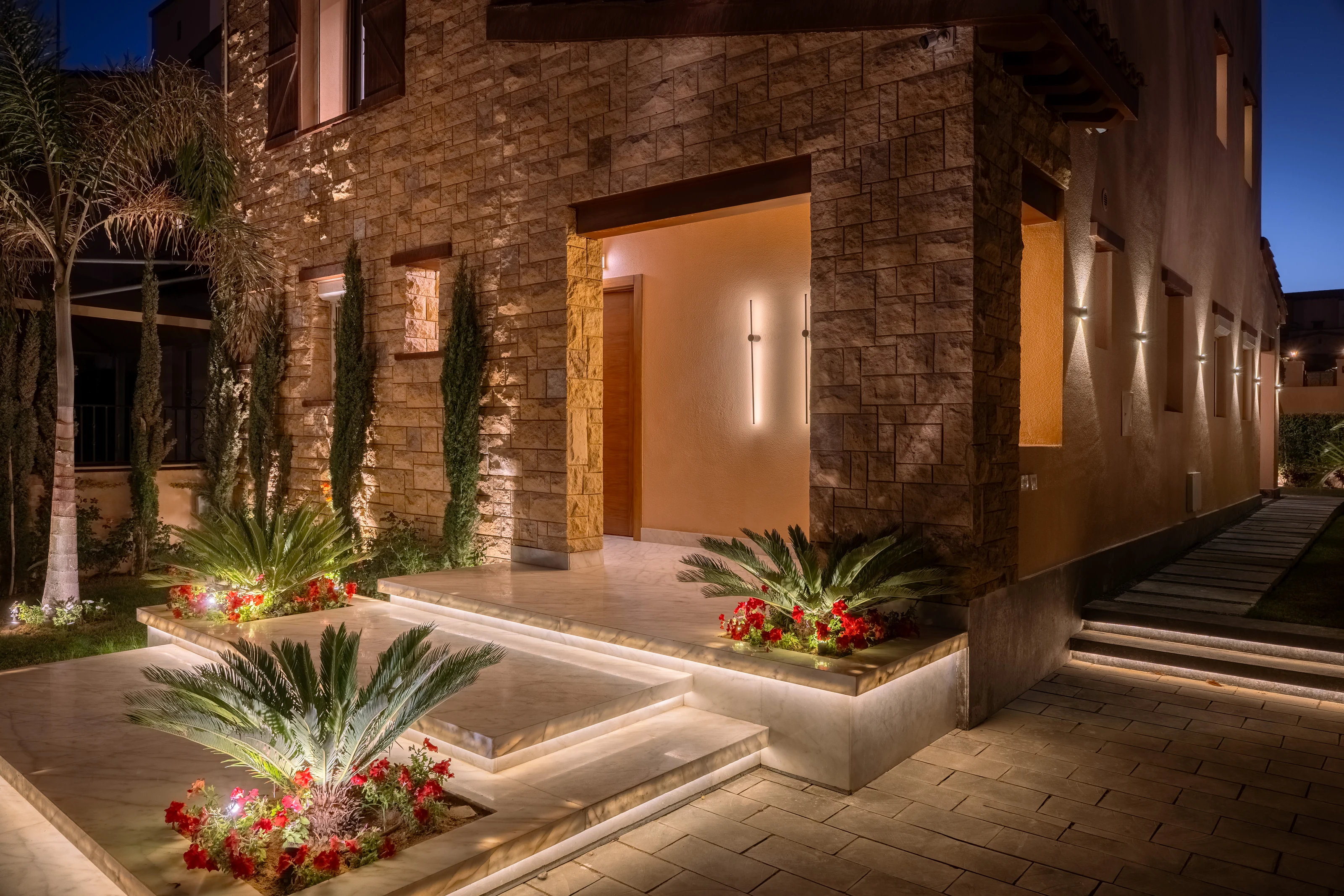 Night view of the Mivida Twin Villa entrance with stone cladding and landscape lighting.