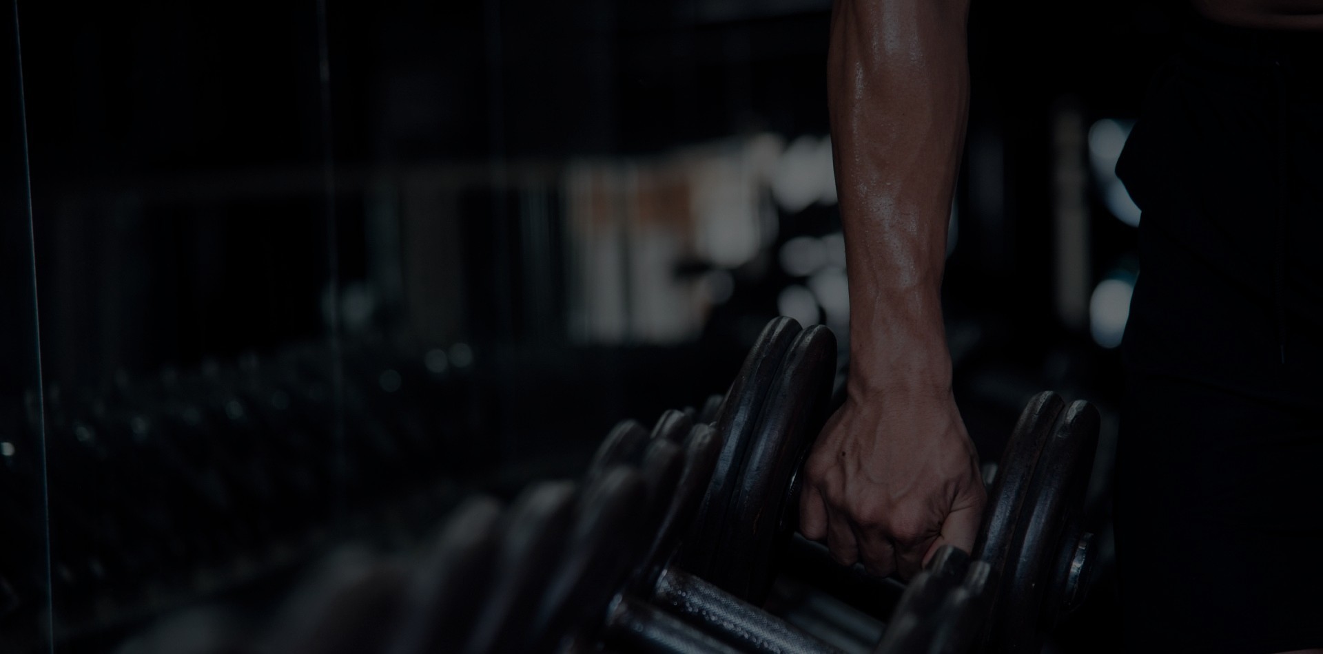 Homem dentro de academia, pegando pesos para iniciar atividades físicas.