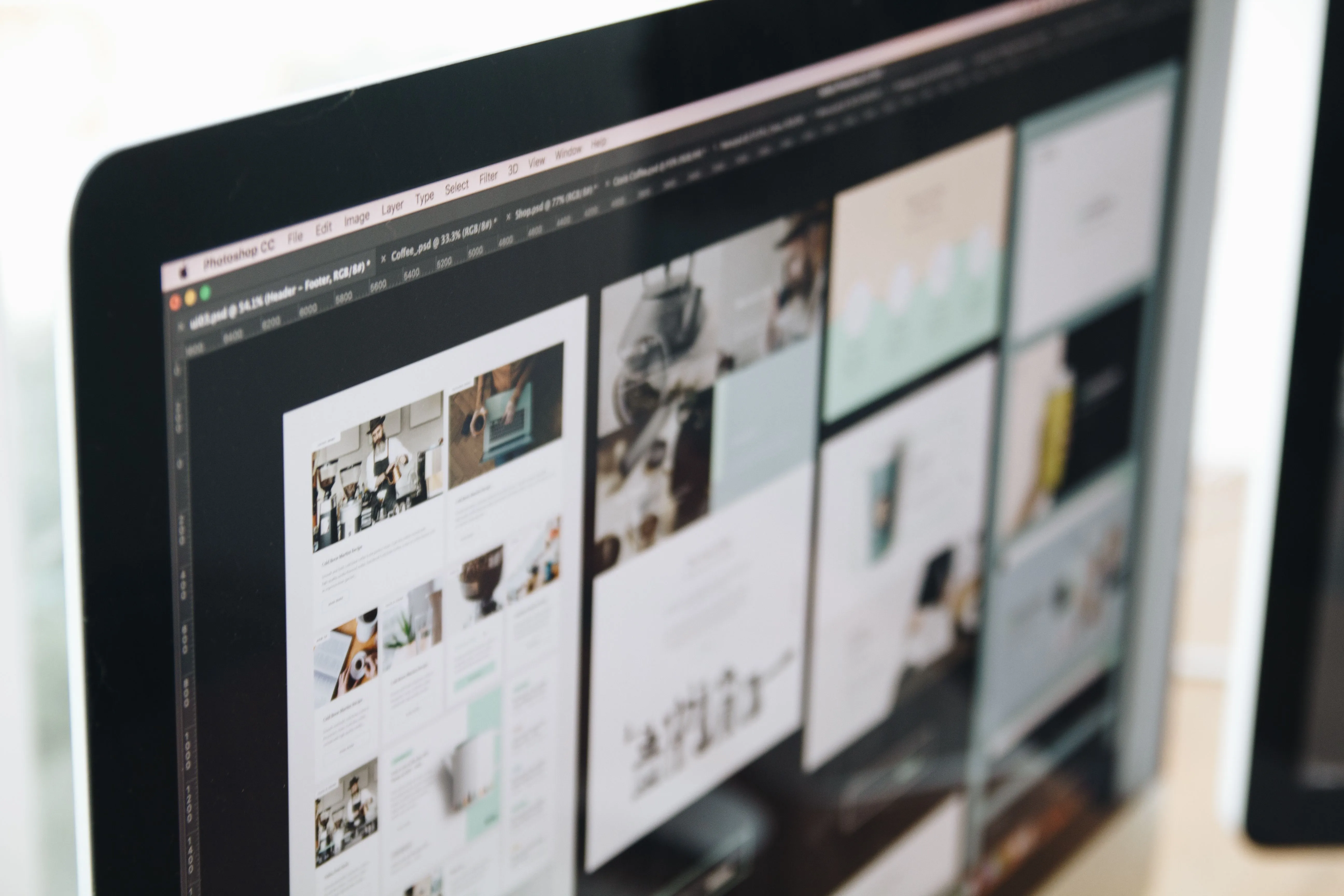 A computer monitor displays a design software interface with multiple project panels showcasing various layouts and graphic designs, encompassing photography, illustrations, and text elements, reflecting a creative workspace.