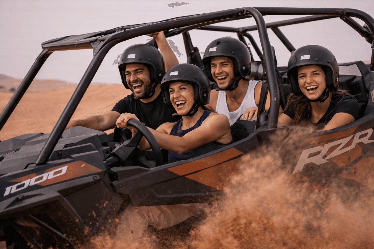 A group of friends laughing and driving a Polaris RZR 1000cc 4-seater through the sand dunes with Dune Quest Tours