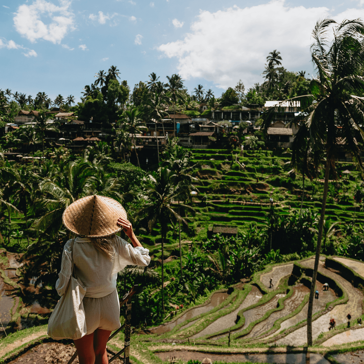 Person in a conical hat looking out over terraced rice fields in Bali, Indonesia