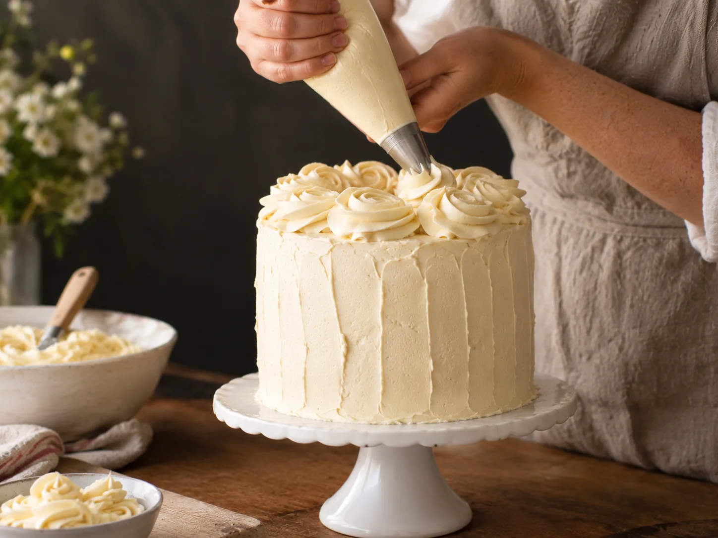Piping buttercream roses onto a tall cake