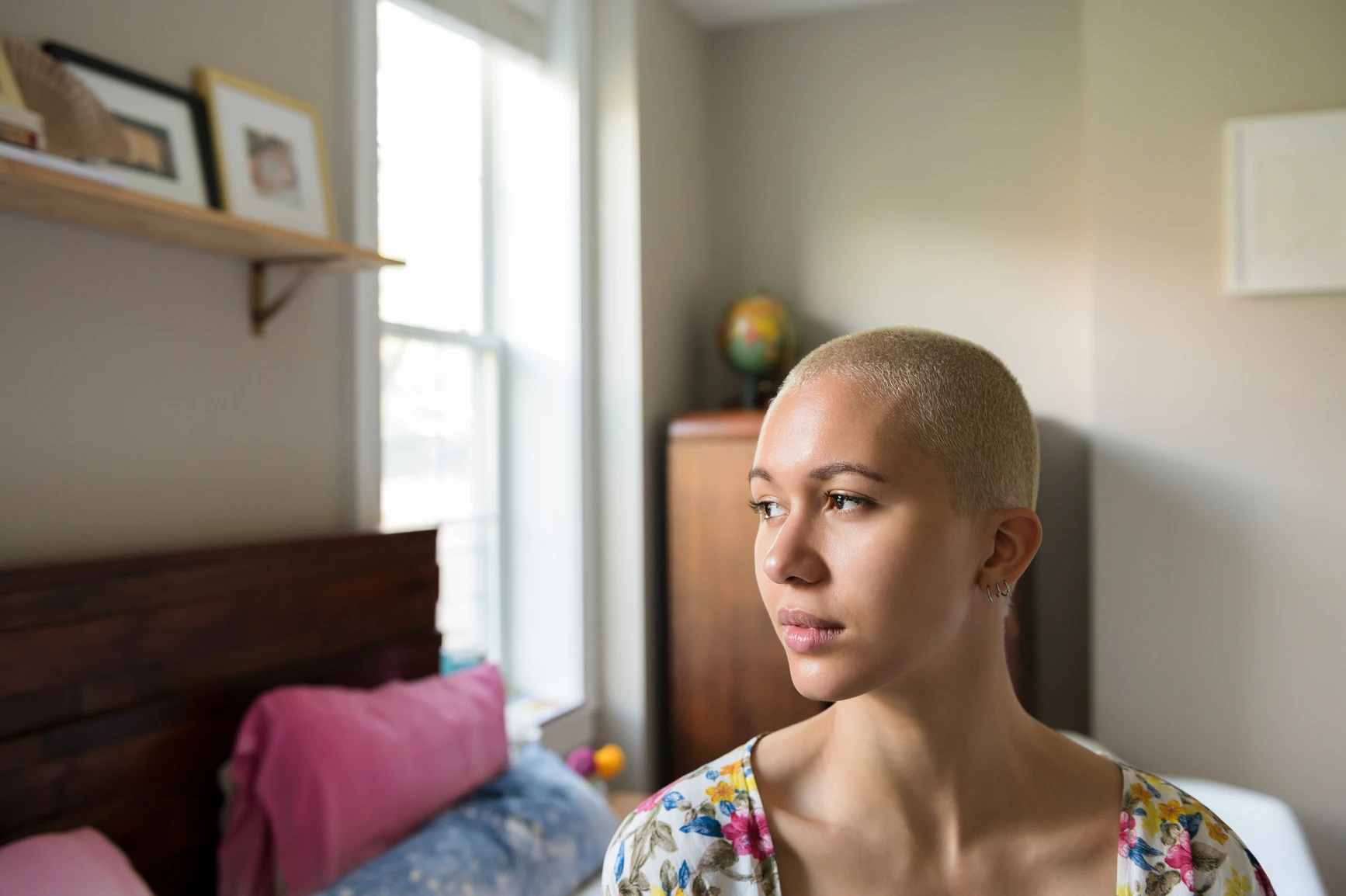 A person with a shaved head sitting calmly in a softly lit room, reflecting inwardly, representing queer therapy themes of shame, self-reflection, and compassion.