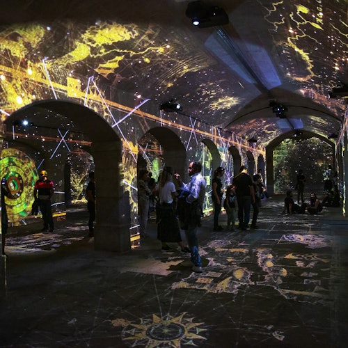 人们在一个拱形的房间里走动和坐着,墙壁、天花板和地板上投射着复杂的灯光,创造出一种神秘的氛围。