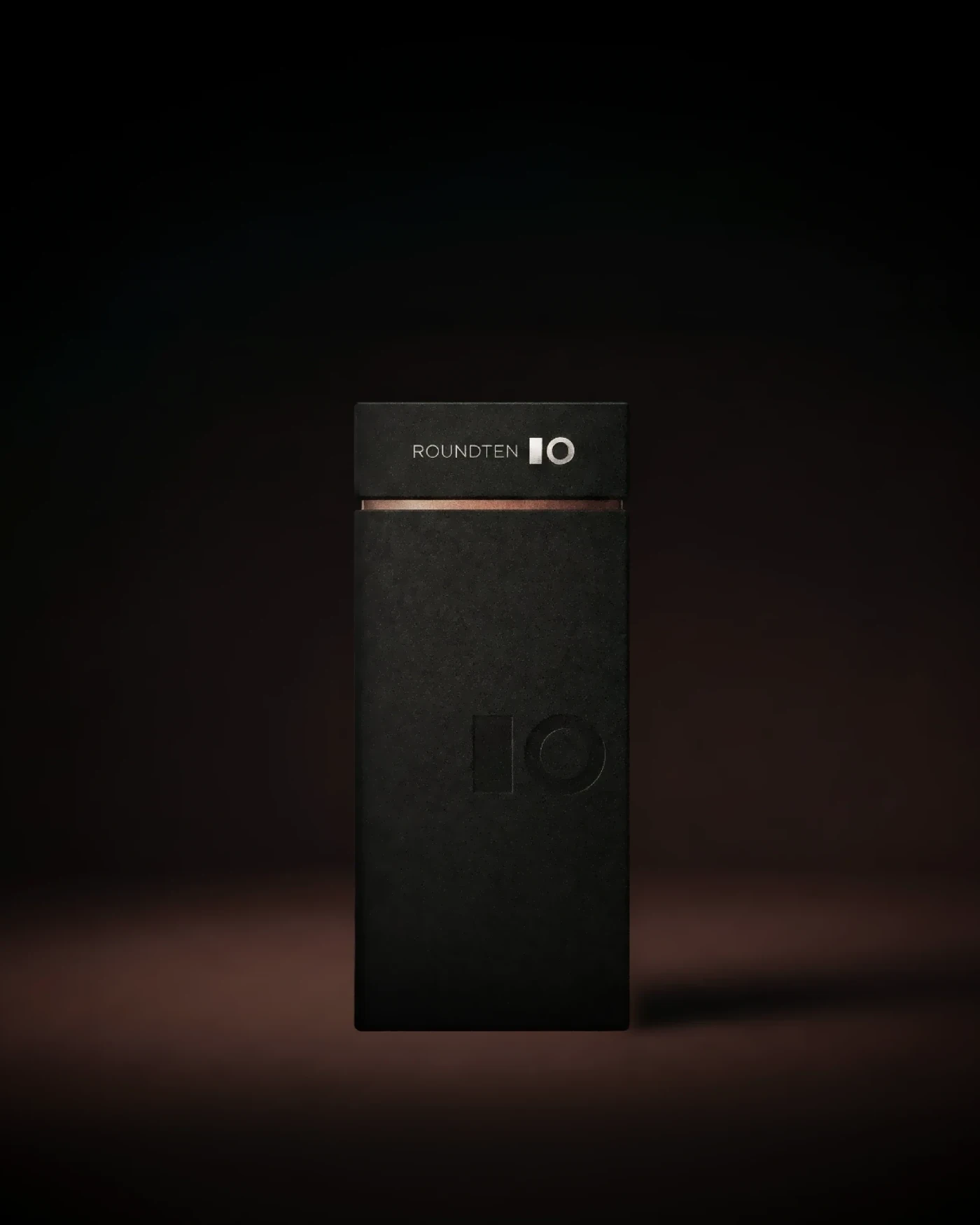 Single black Roundten box with a bronze band and the 10 logo on a dark background, packaging design by Sebastian Saavedra