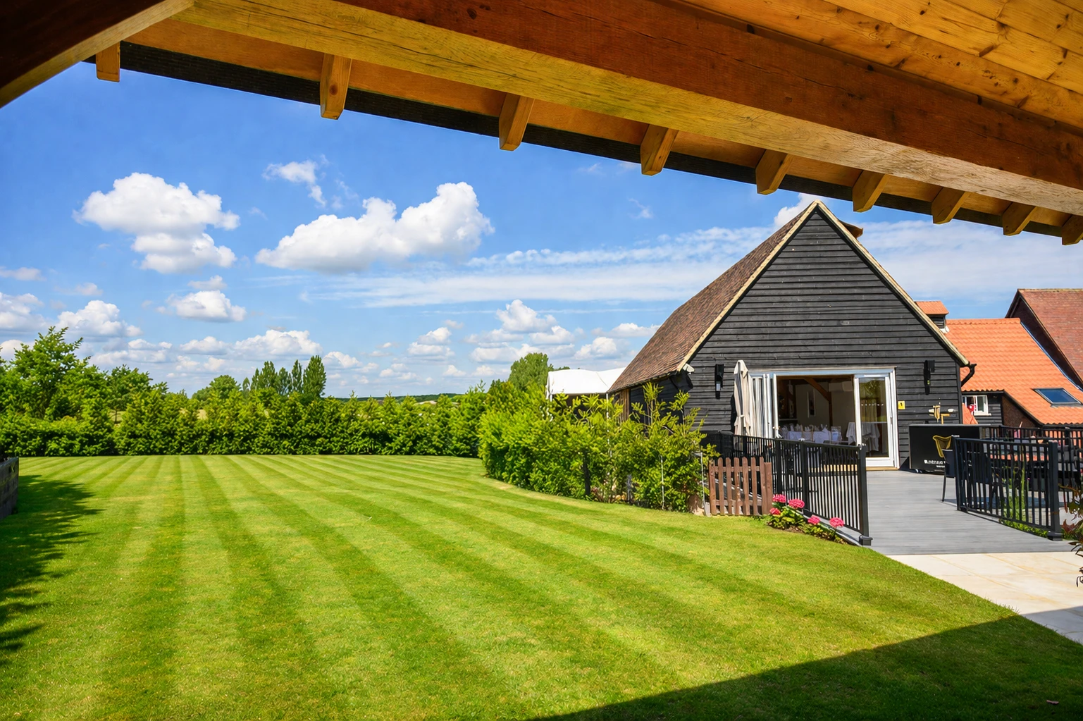 Wooden barn building with open doors, gray deck & patio seating.