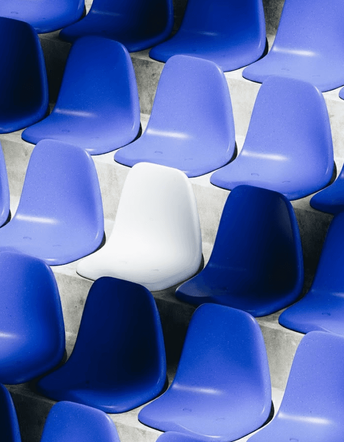 Rows of light and dark blue stadium seats on concrete steps with a single white chair standing out.
