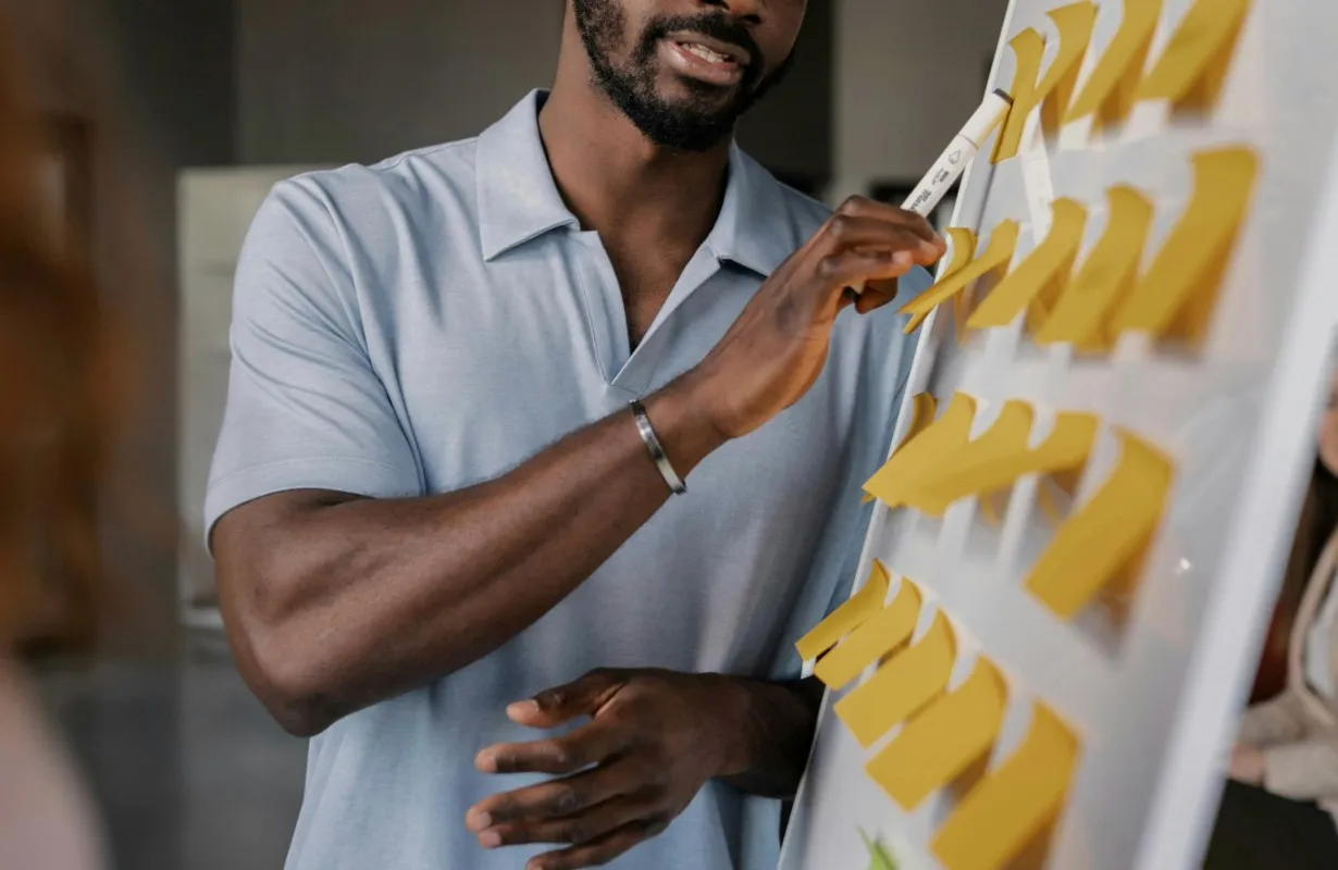 A Black man pointing at sticky notes on a whiteboard during a presentation. Business strategy.