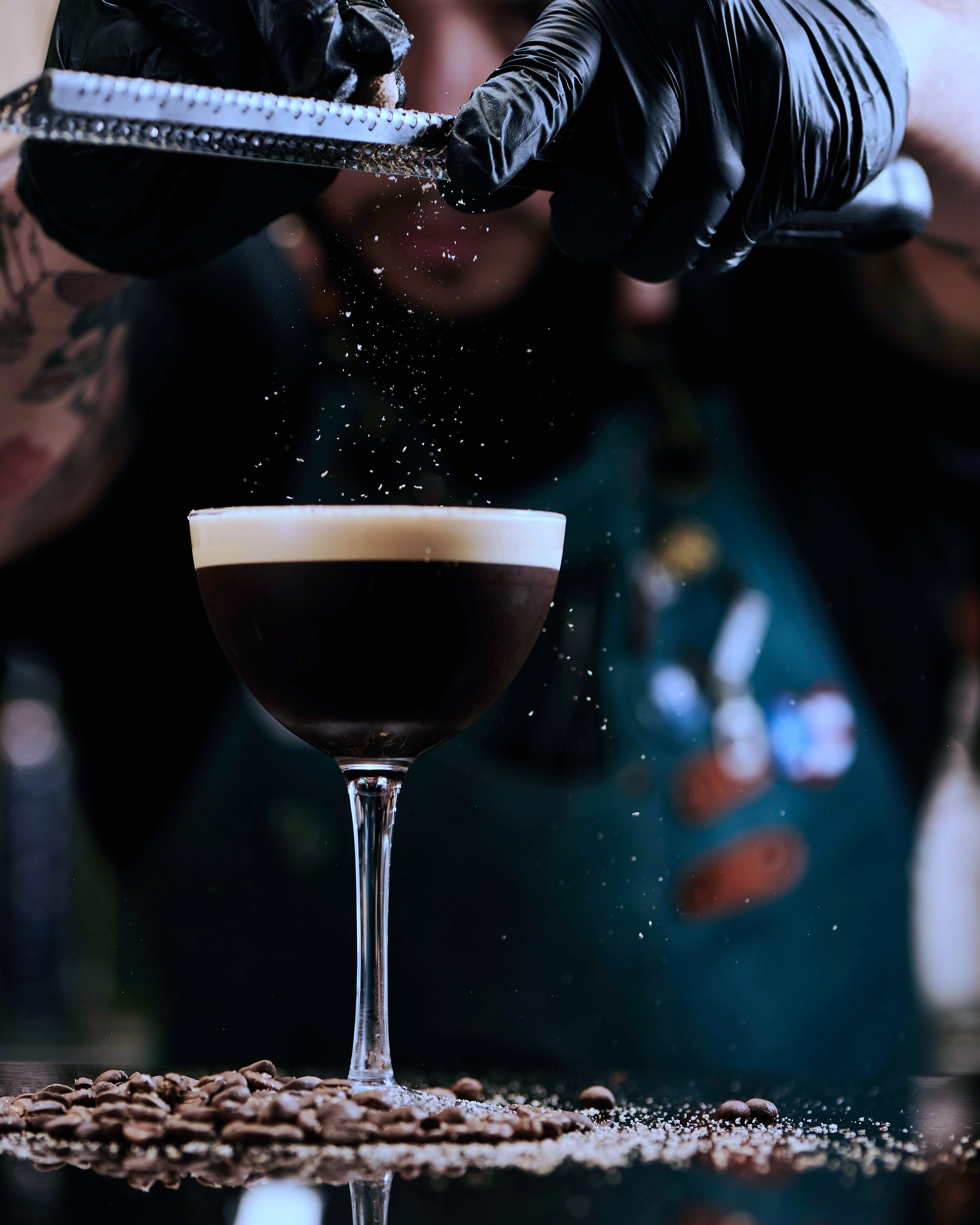 Mixologist grating fresh espresso beans on an espresso martini.