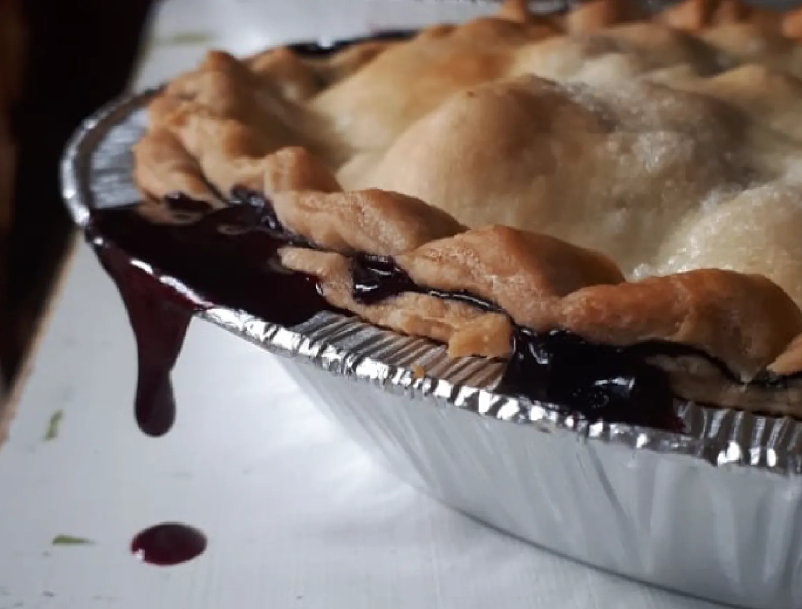 A close up of a berry pie with juice dripping off the side of the pie tin.