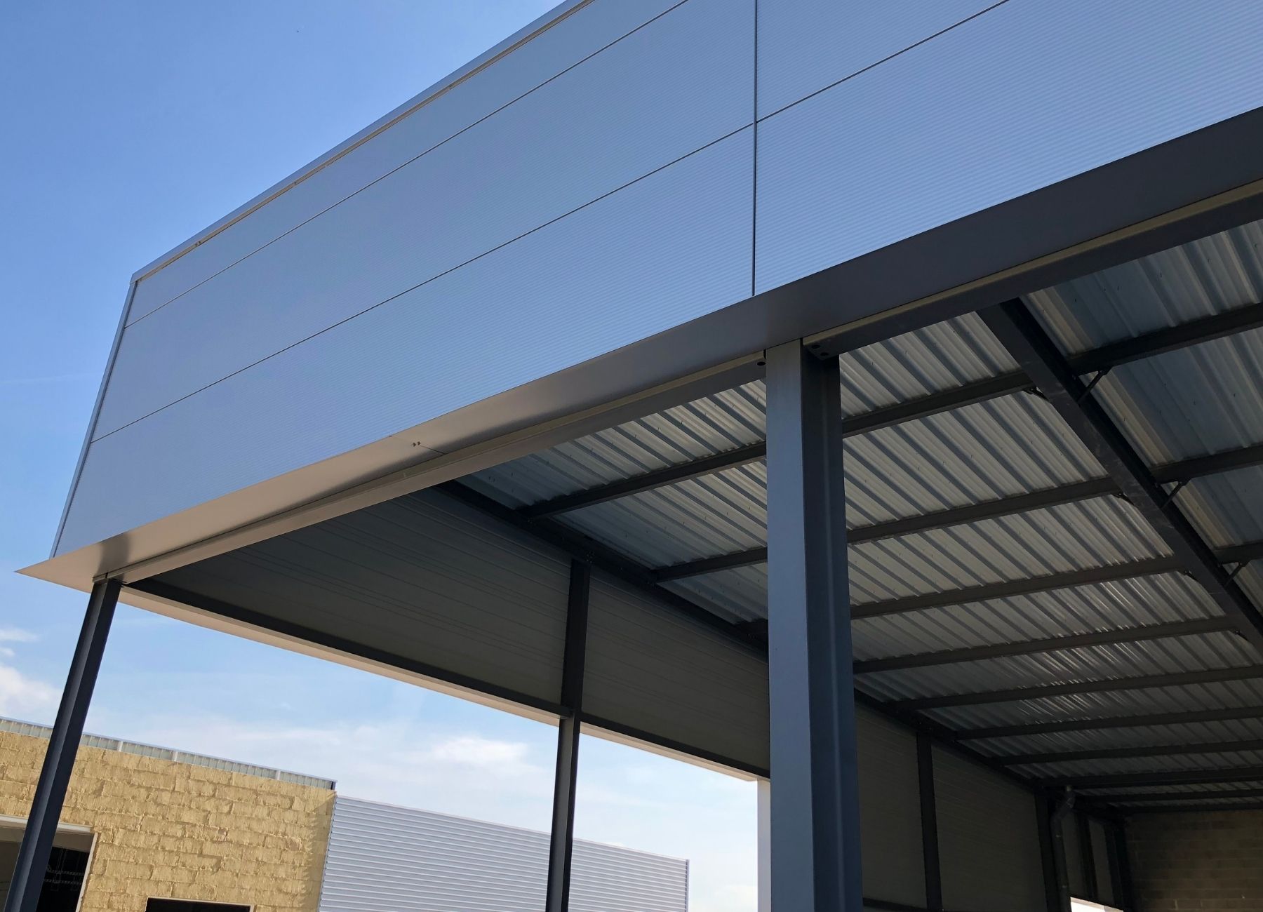 Auvent métallique avec bardage en tôle nervurée et poteaux en acier, vue en contre-plongée.