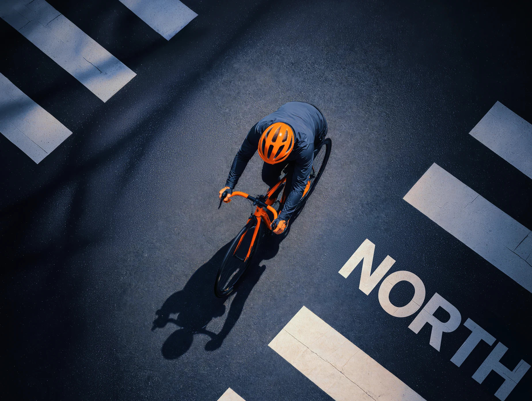 Top-down view of a cyclist riding an orange North bike across bold street markings.