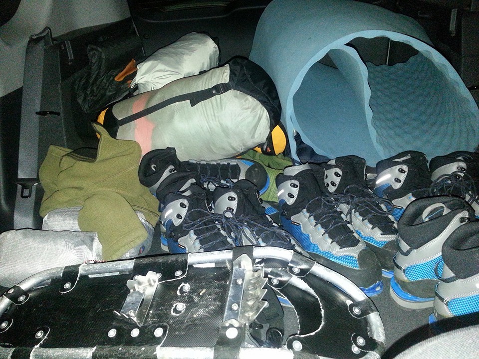 a pile of boots, snowshoes, and camping gear sits in the trunk of a vehicle