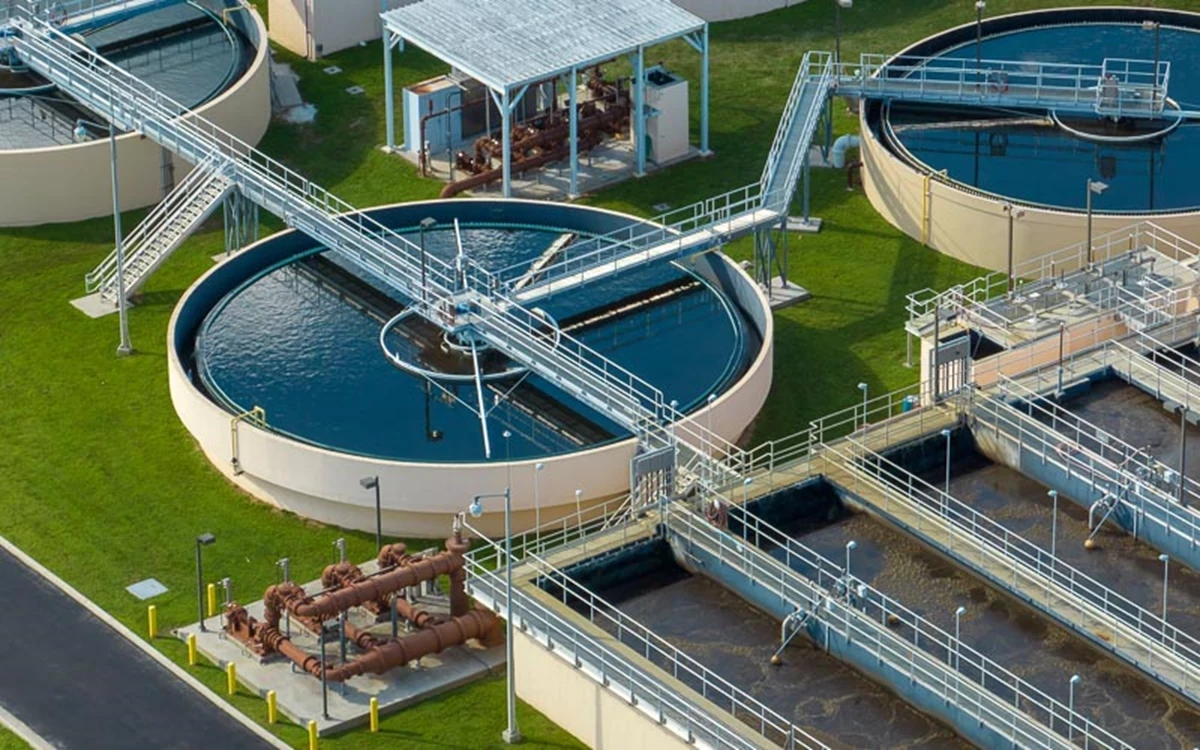 Aerial view of a wastewater treatment plant with circular clarifiers, rectangular settling tanks, and connecting metal walkways.