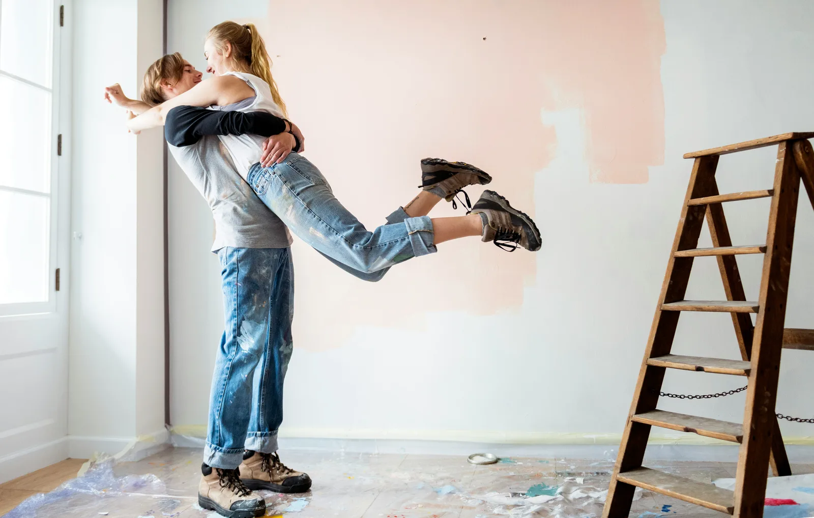 Joyful couple celebrating while painting room, man lifting woman