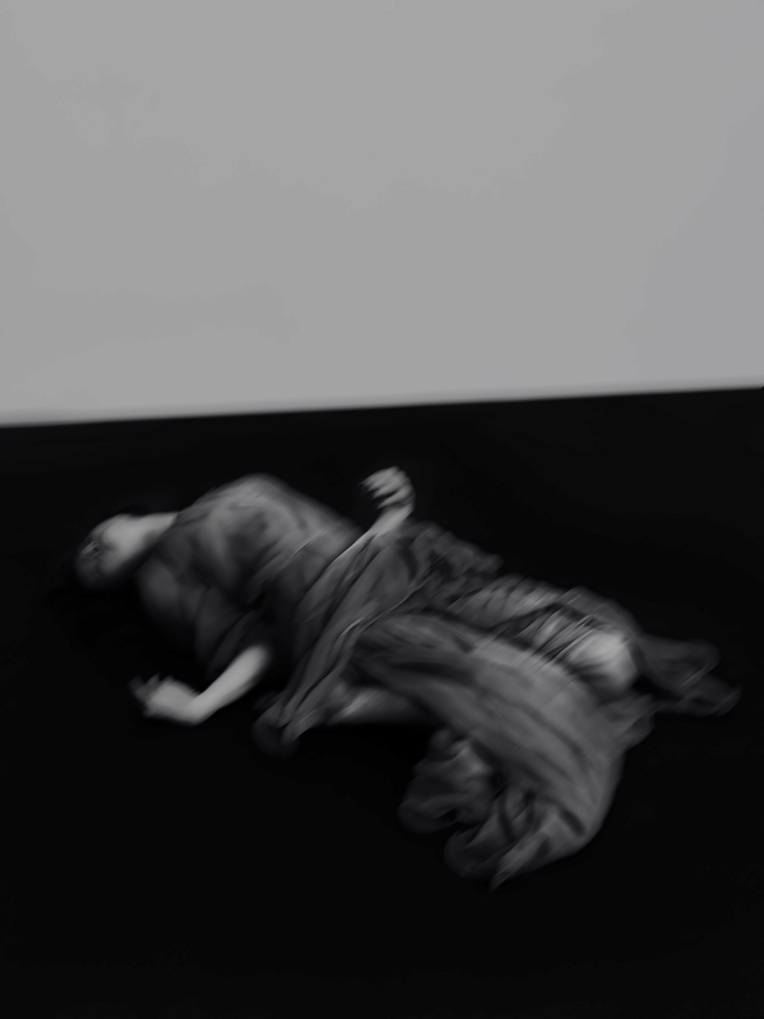 A modern photographic editorial black and white portrait of a woman laying on the floor. She is in a contorted and expressive pose. There is motion blur in the image to enhance dramatic effect. 