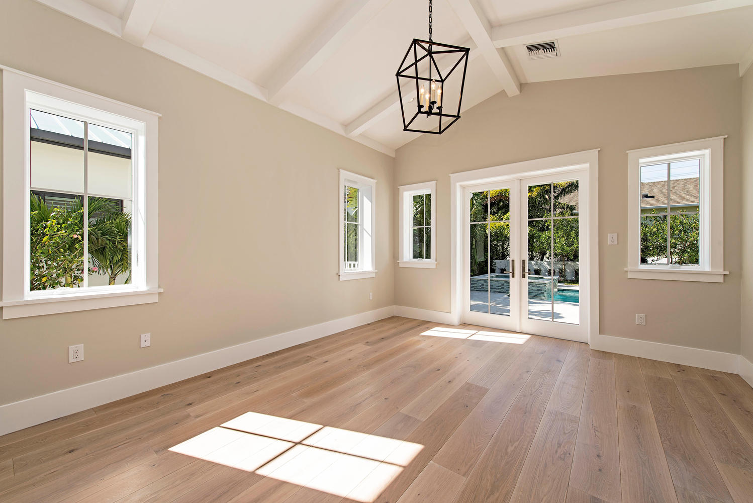 a large open room with multiple windows, glass frame doors, and light wood flooring