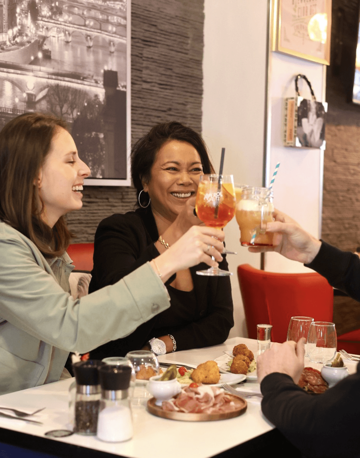 Wooden outdoor table set with multiple plates of food, including dips, salads, potatoes with cheese, and glasses of water, with hands reaching in to eat.