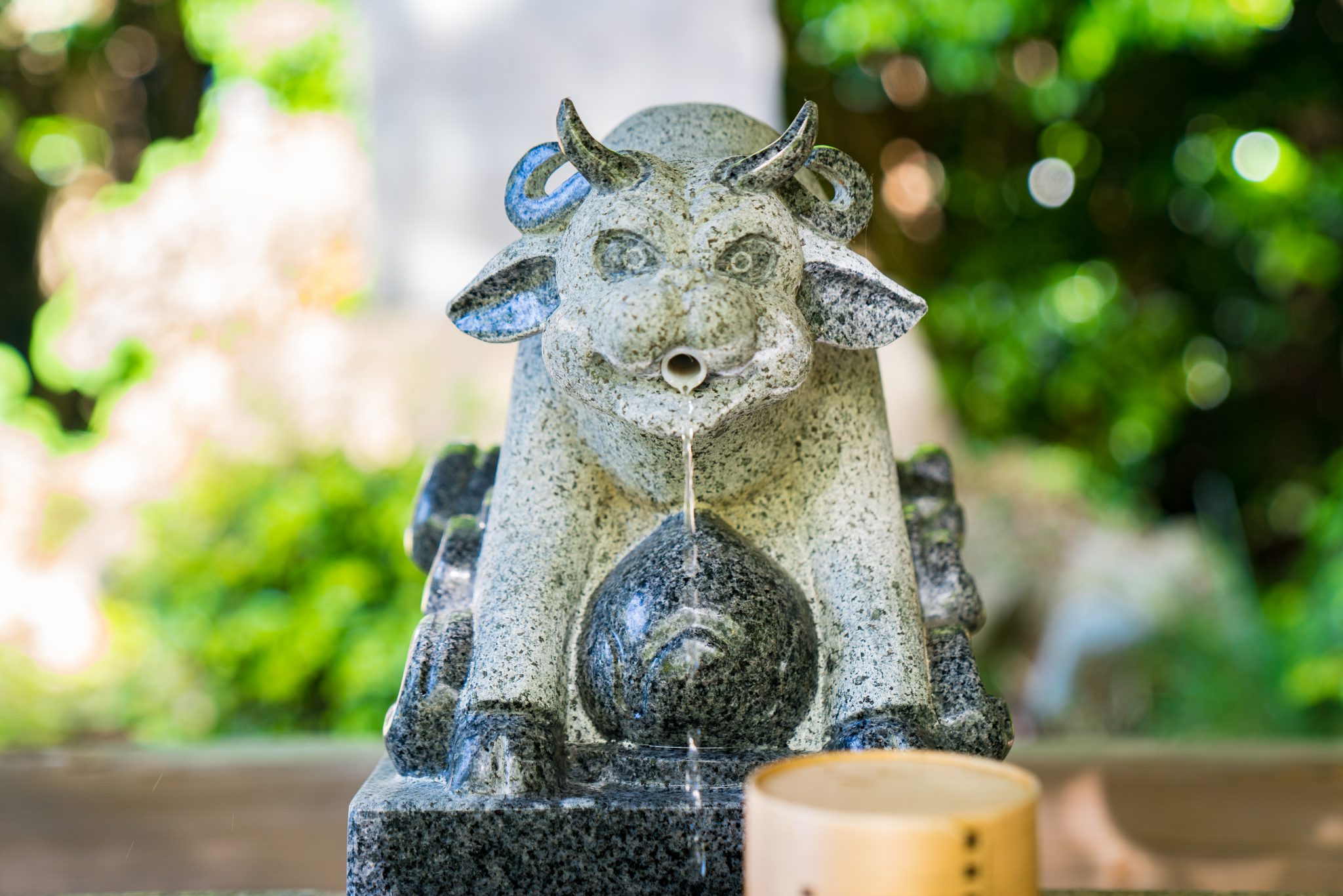 A temple fountain shaped like a cow, with water gently flowing from its nose into a stone basin below.