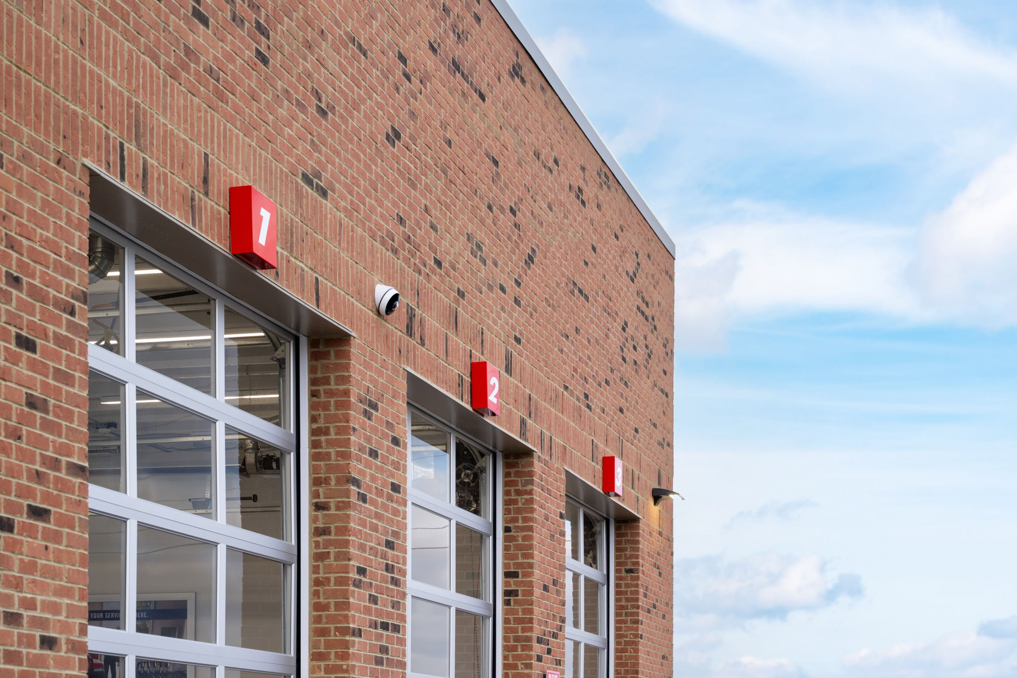 Close-up of a high-end commercial facade featuring grey stacked stone veneer, vertical red architectural slats, and horizontal wood-grain siding installed by Kith Exteriors.