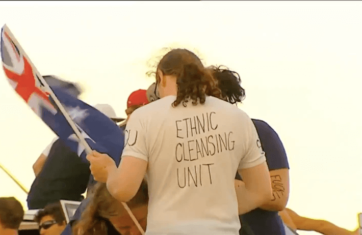 A still from the video shared by Australian neo-Nazis about the Bondi Beach shooting, showing a man holding an Australian flag wearing a shirt that reads "Ethnic Cleansing Unit."