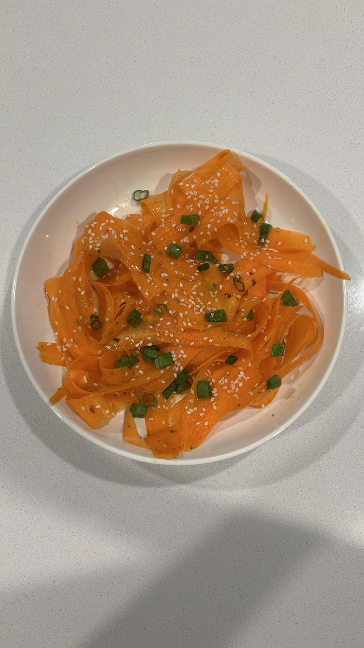 Shaved carrot salad ribbons with sesame seeds and green onion in white bowl – light carrot ribbon salad side dish Wellness by Suhey