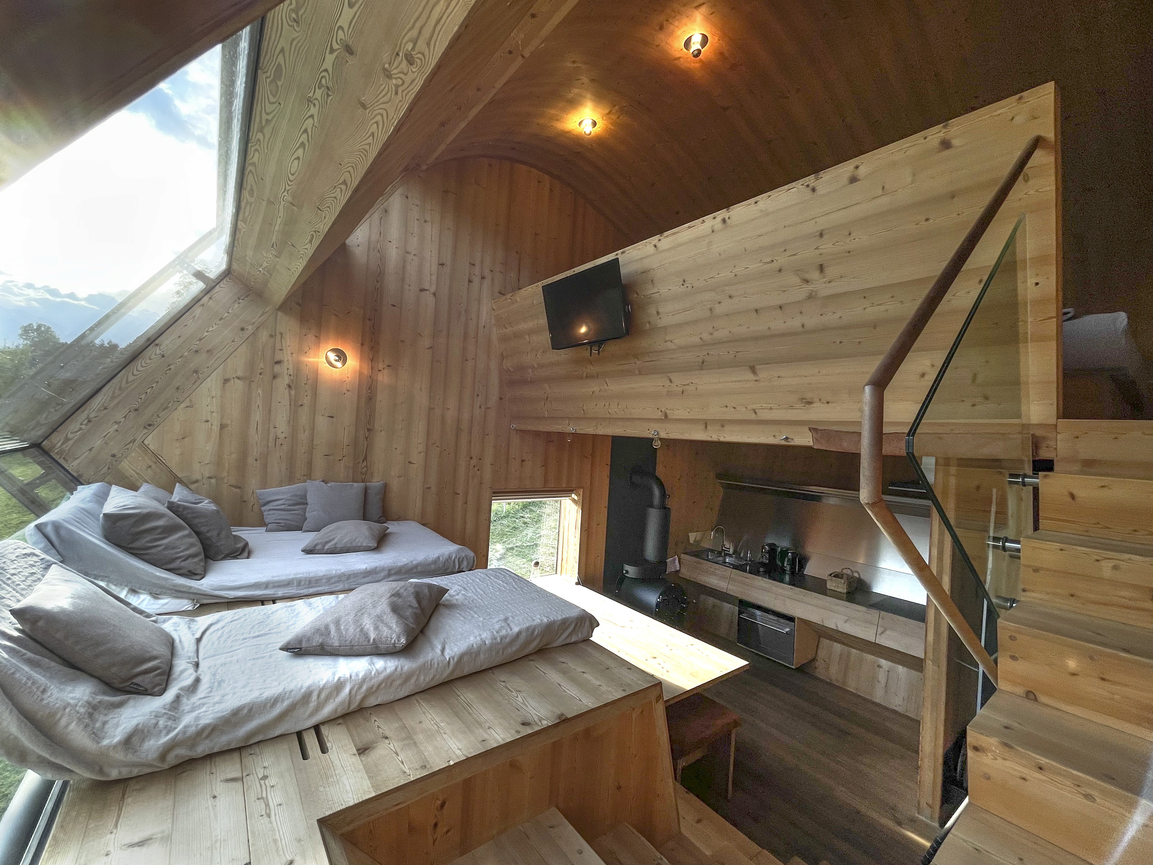 Warm wood-lined living space at Ufogel with panoramic window, mezzanine bedroom, and compact kitchen