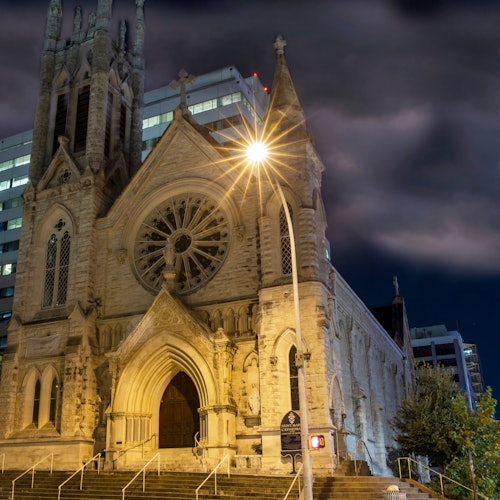 Tall church cathedral at night with a light shining from behind it.